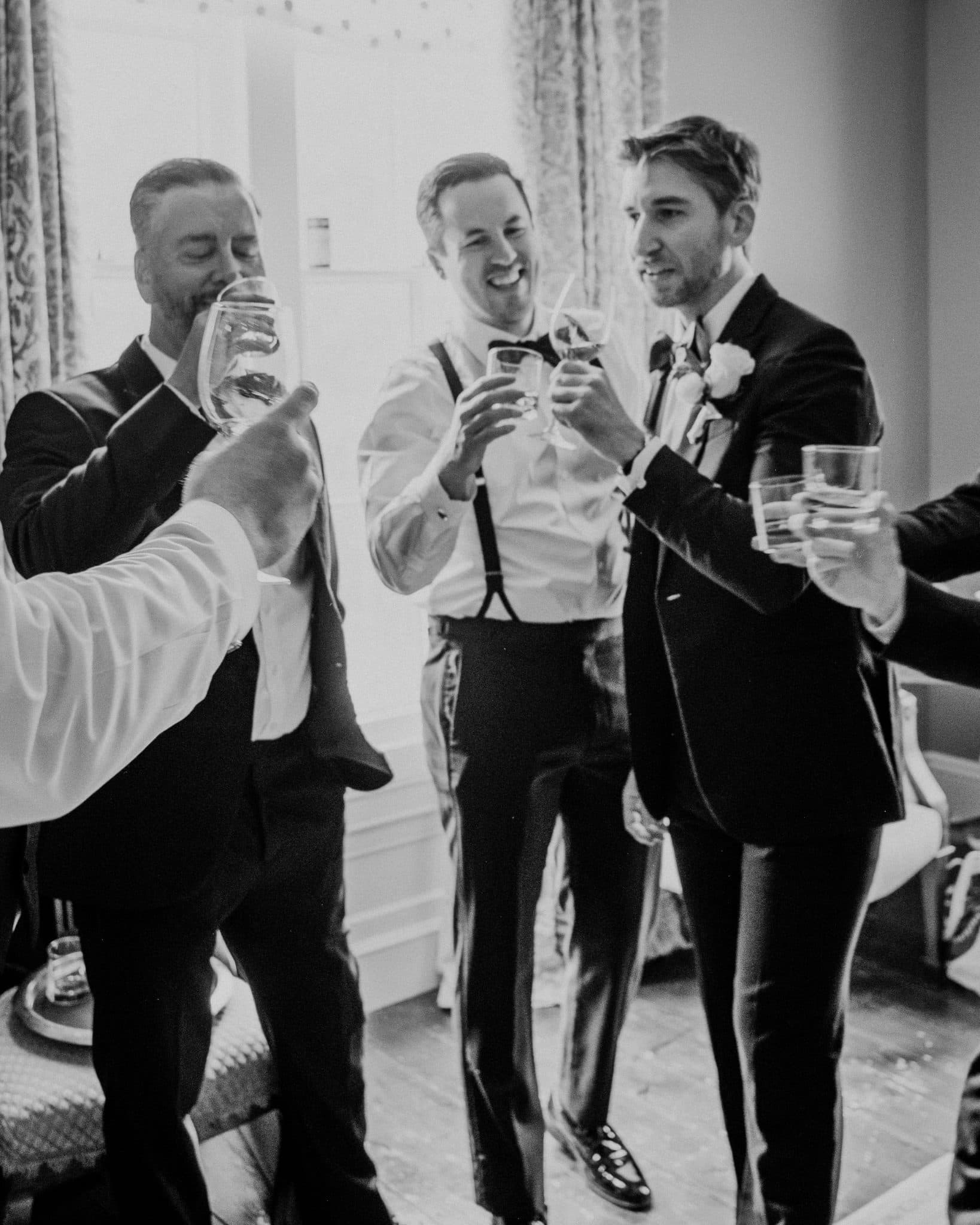 A group of men in formal attire raise glasses in a toast, smiling and celebrating.