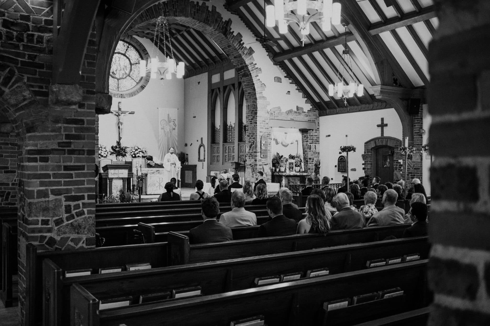 A black and white wedding photograph shows a church interior with pews, a priest at the altar, and a congregation seated facing forward.