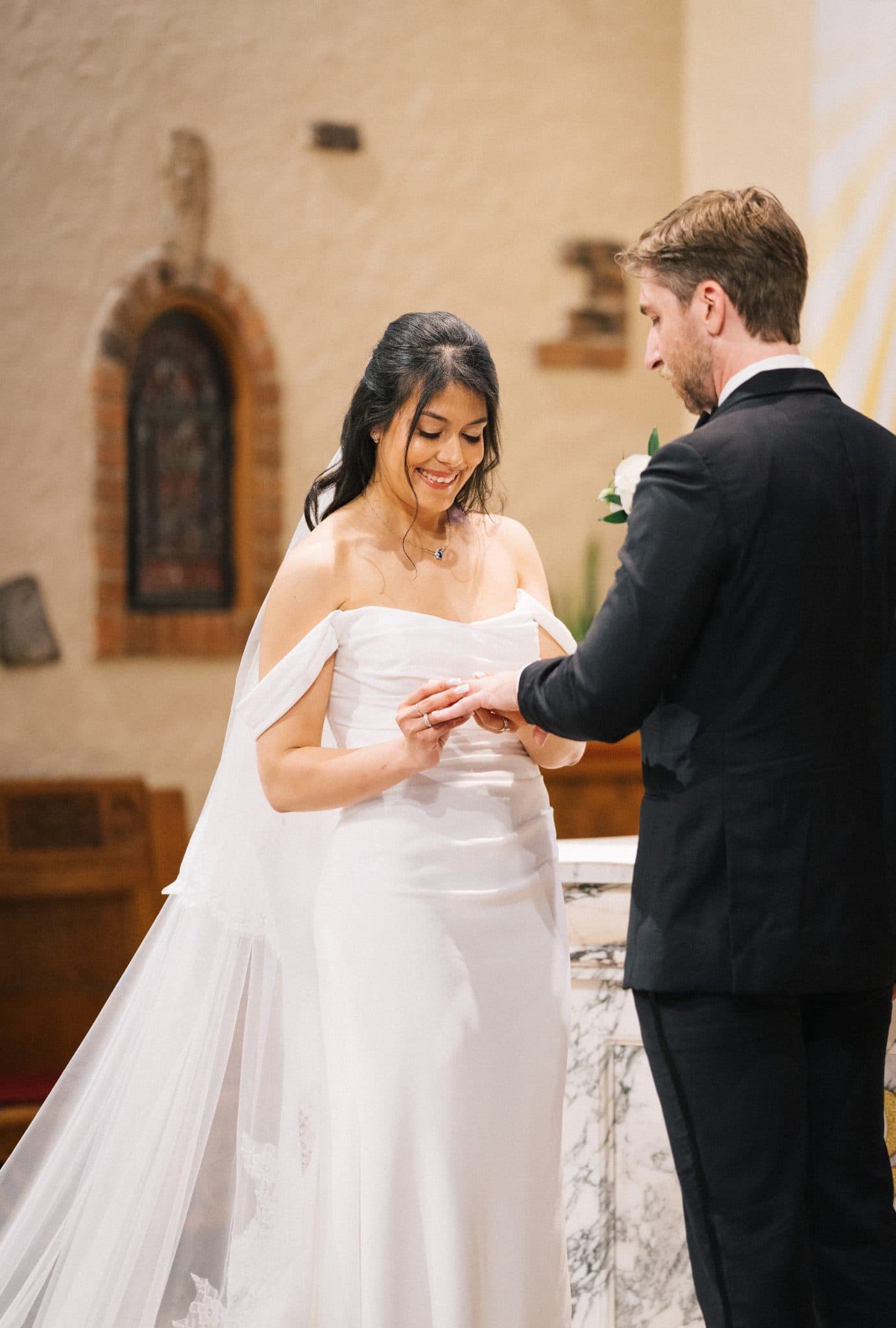A bride in a white dress and veil stands at a church altar, exchanging rings with a man in a black suit.
