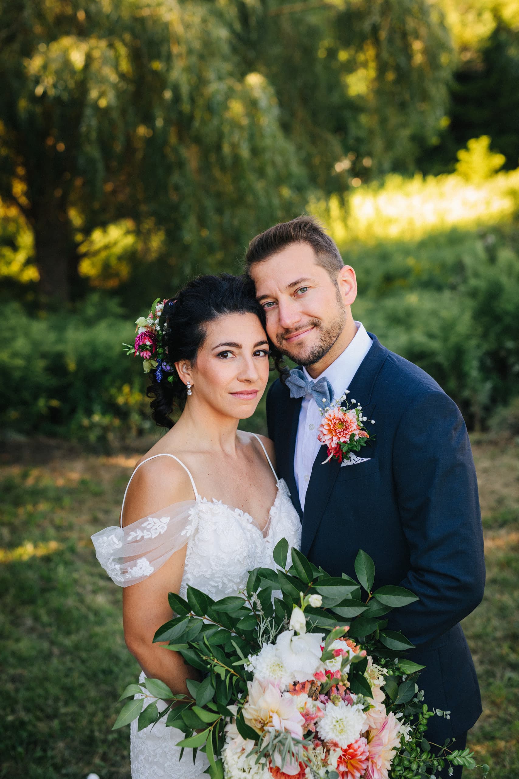 Bride and groom smiling cheek to cheek behind a bouquet of dahlias and greenery