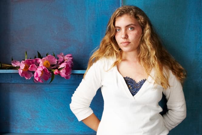 A teenage Beth in front of a blue backdrop with pink peonies, from her high school photography internship.