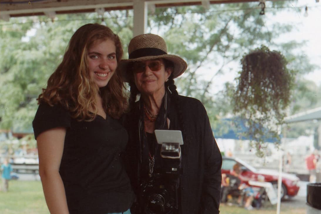 A young Beth arm in arm with the documentary photographer Mary Ellen Mark, who wears a straw hat with a camera around her neck, at an outdoor workshop.