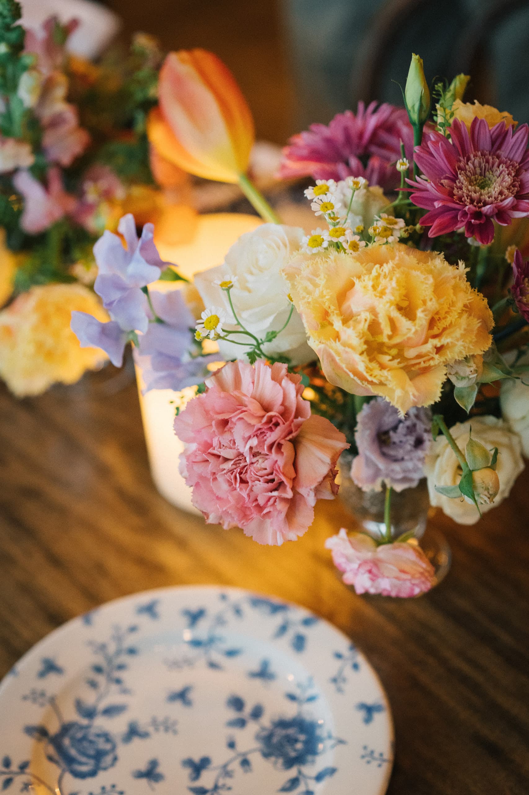 Spring bud vases of carnations, roses, and sweet peas beside a blue-and-white china place setting