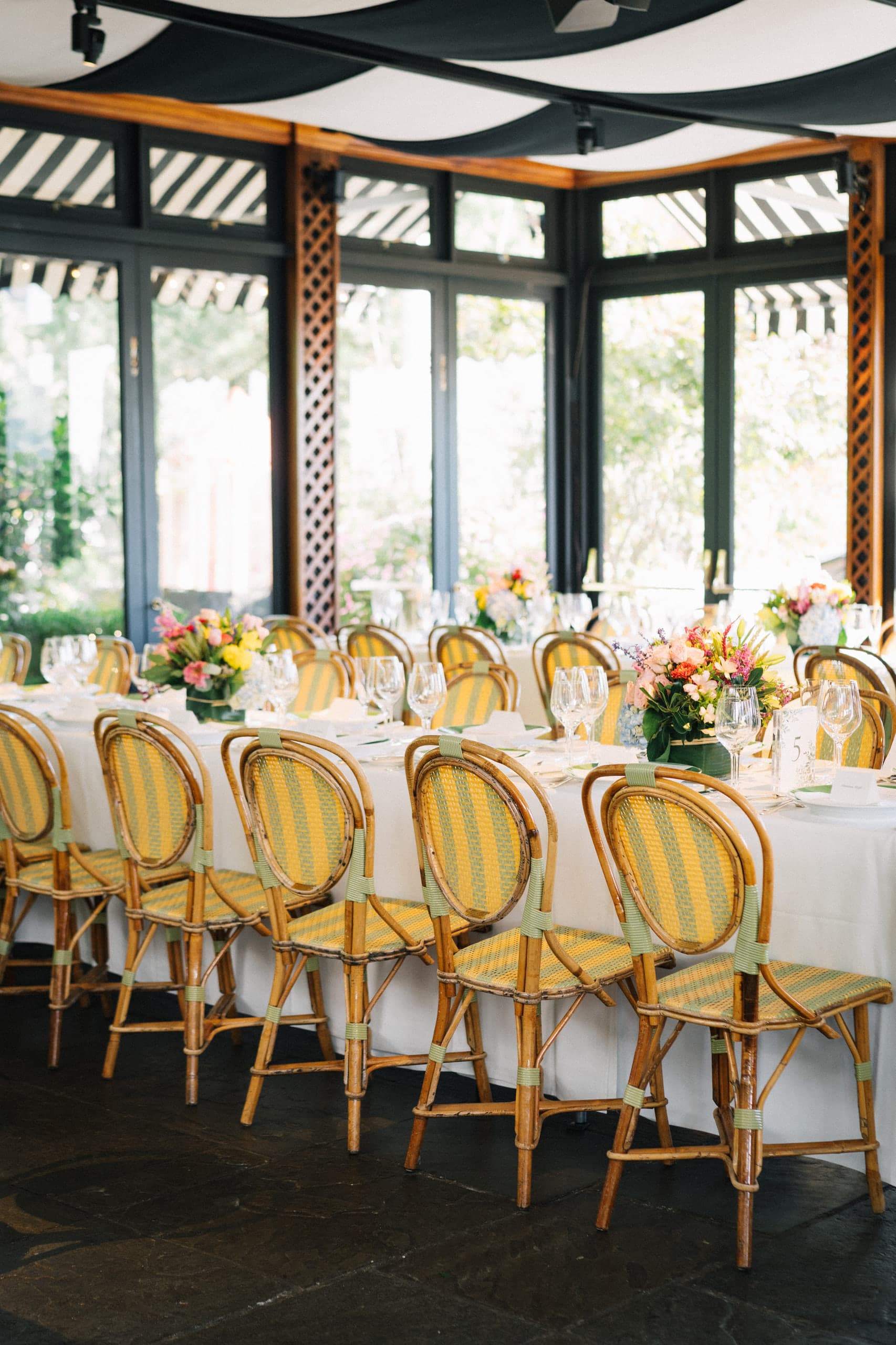 A sunlit reception room with striped bistro chairs and bright centerpieces