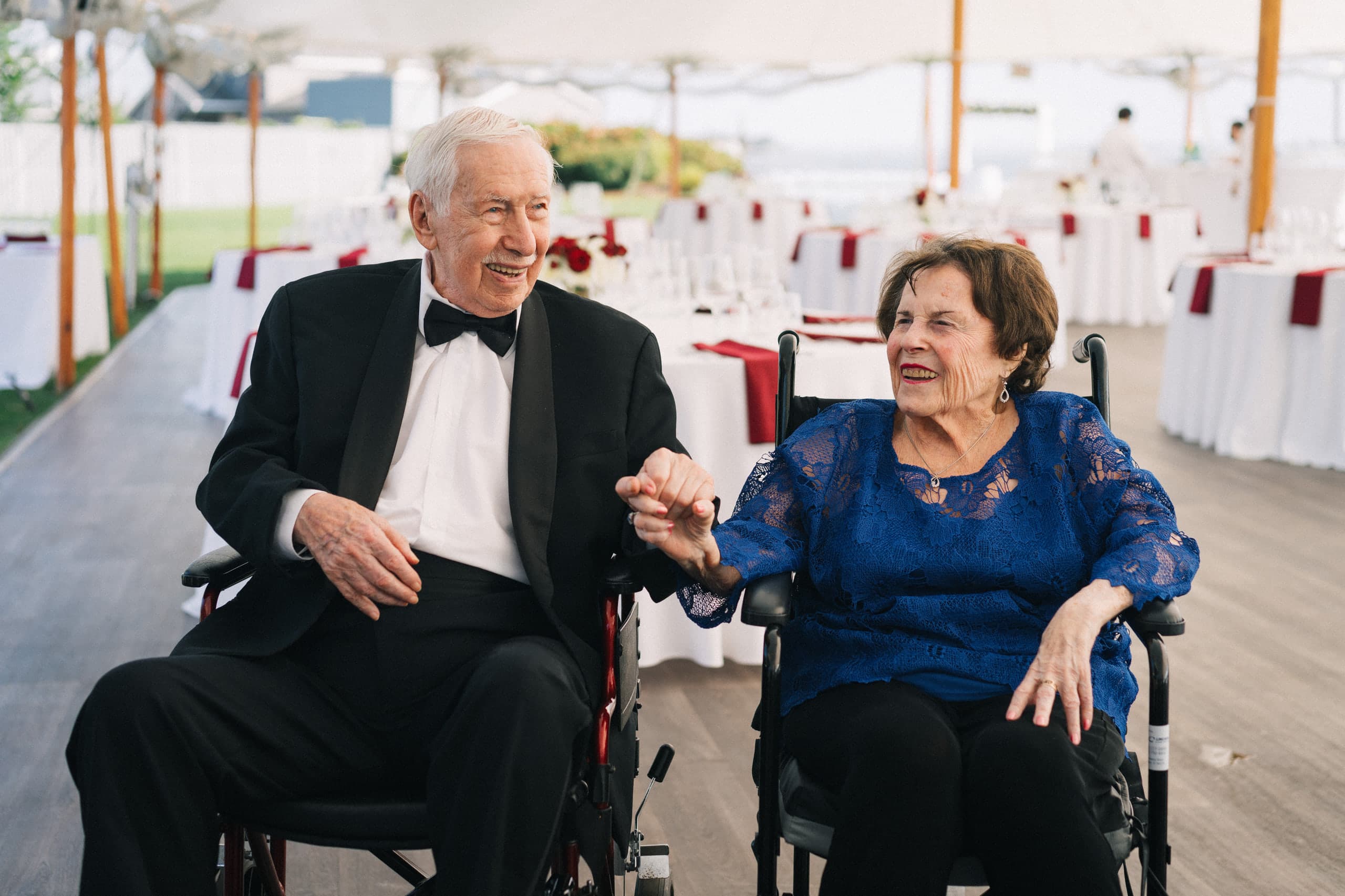 Elderly couple holding hands and laughing at a tented reception
