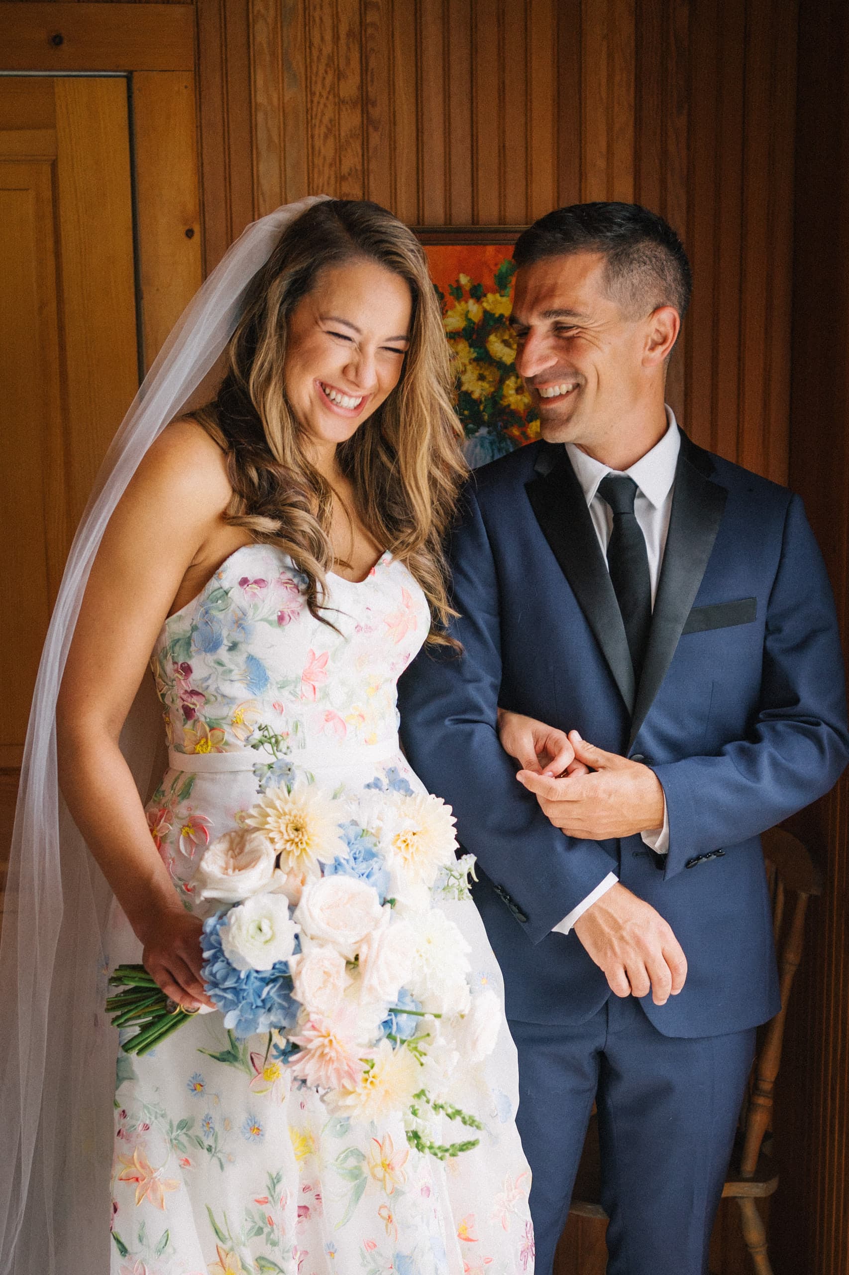 Bride in a floral gown laughing arm in arm with the groom