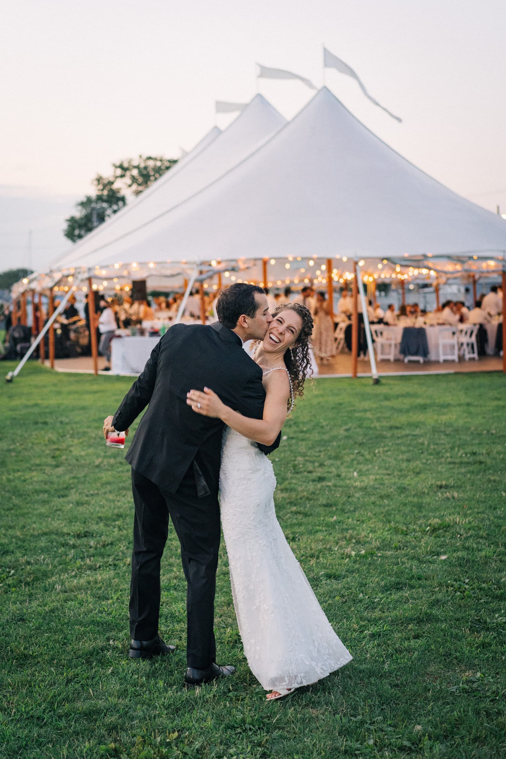Groom kissing the bride's cheek outside a glowing reception tent