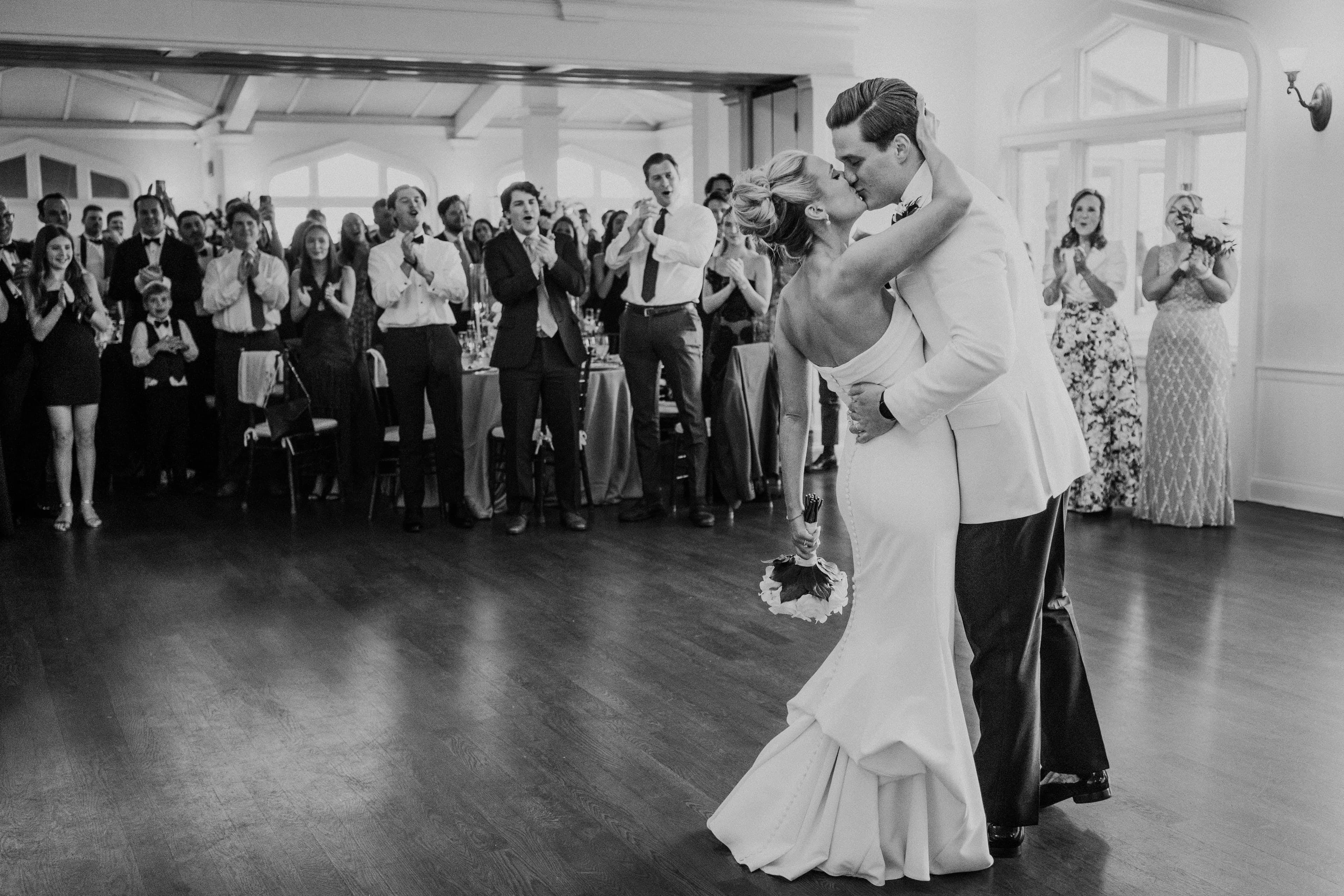 A wedding couple kissing on the dance floor surrounded by guests