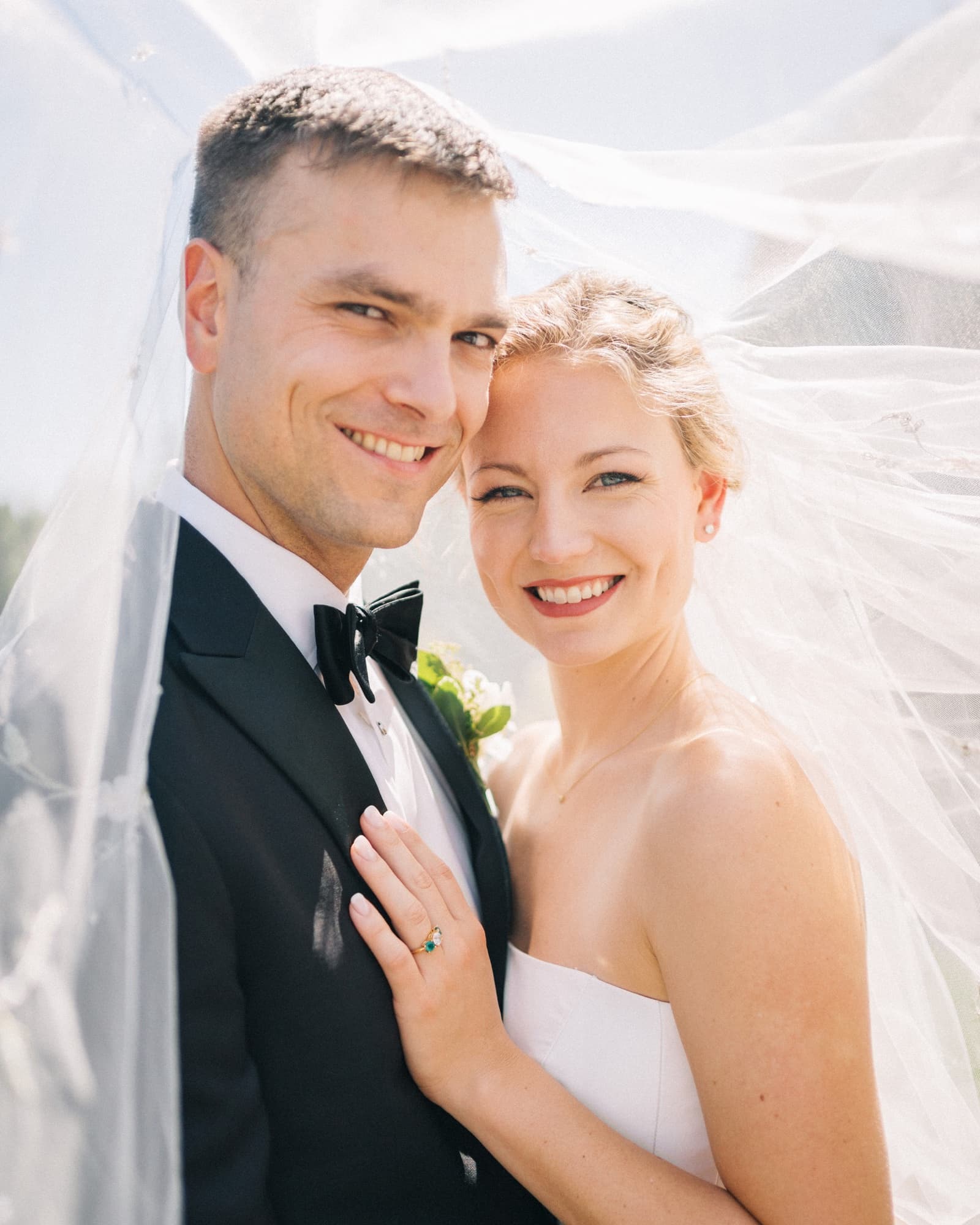 Daryl and Jeff close together beneath a sunlit veil, her hand with an emerald ring resting on his tuxedo lapel
