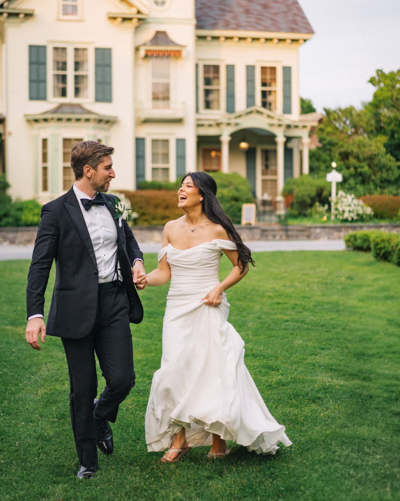 Steph and Chris holding hands and laughing as they walk across the lawn in front of the Jedediah Hawkins Inn