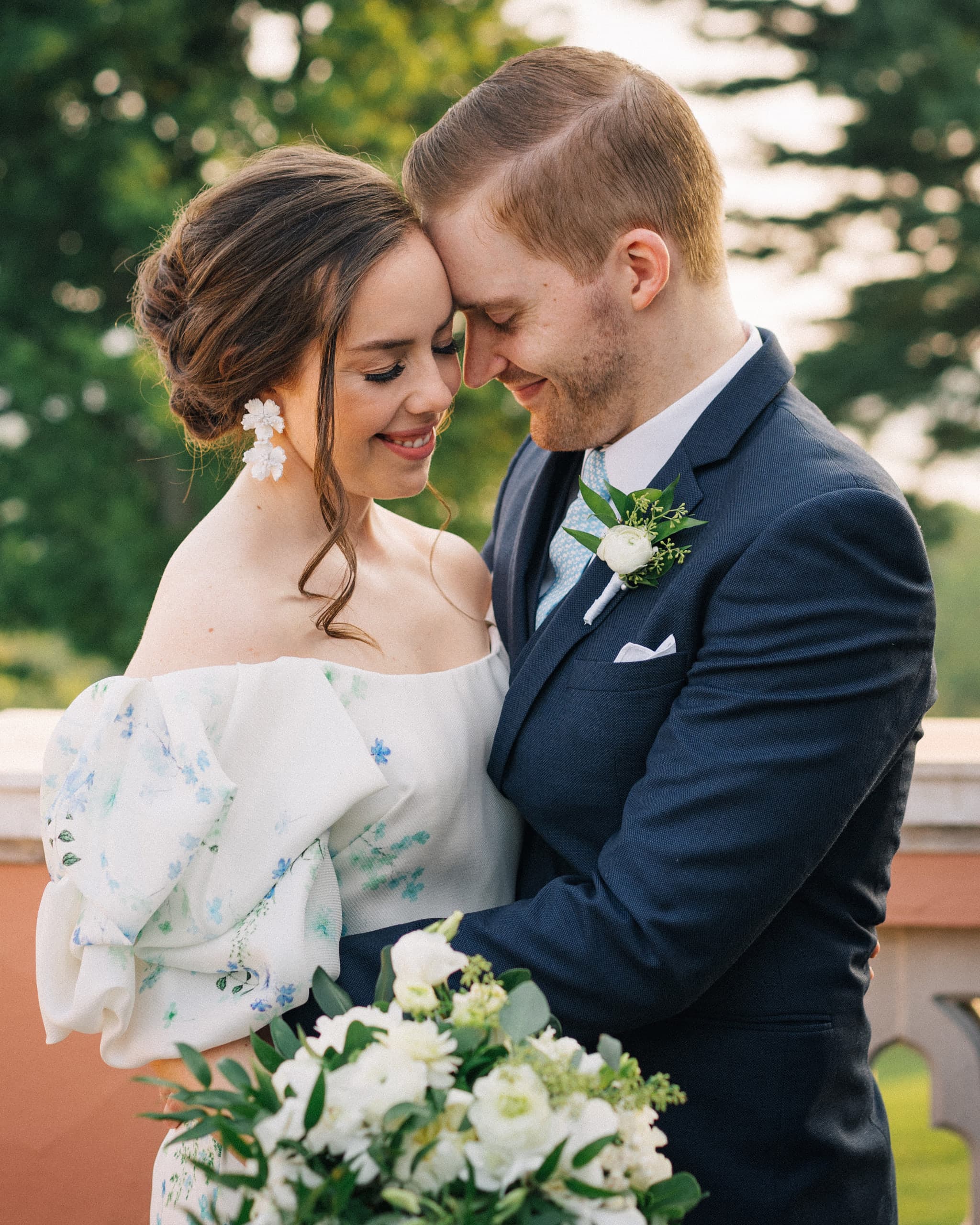 Couple resting their foreheads together on a garden terrace, the bride holding a white bouquet