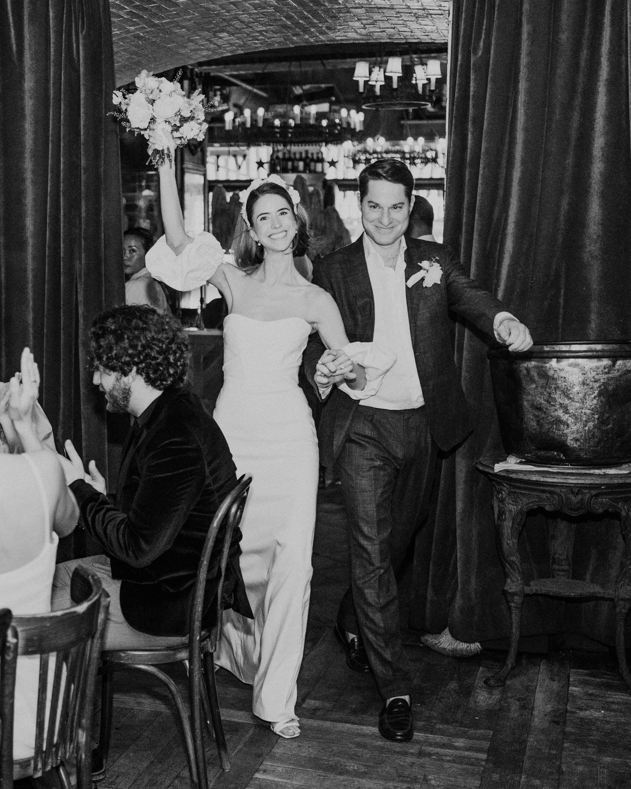 Newlyweds entering their reception through a restaurant, the bride raising her bouquet, in black and white
