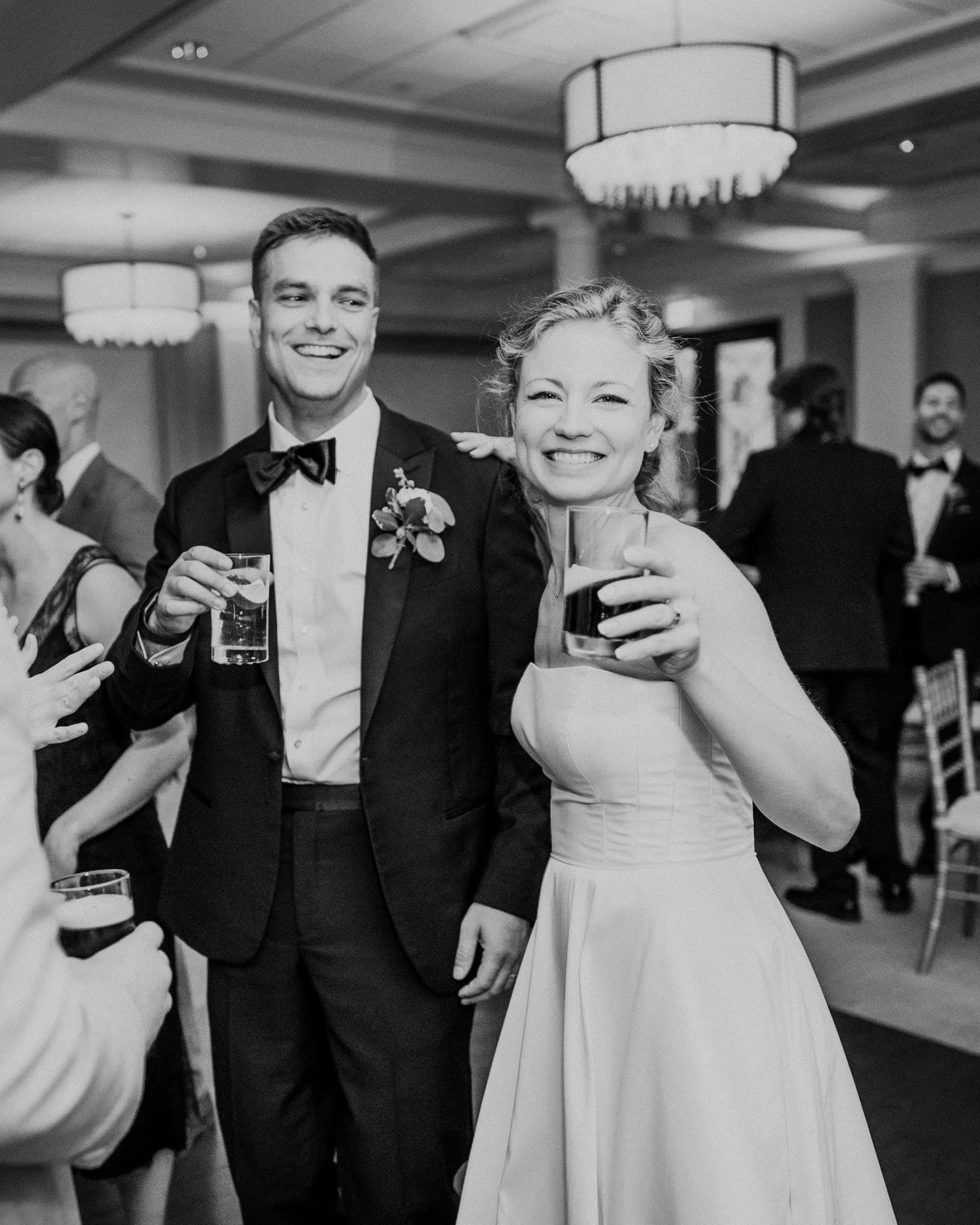 Bride and groom raising drinks together on the dance floor, in black and white