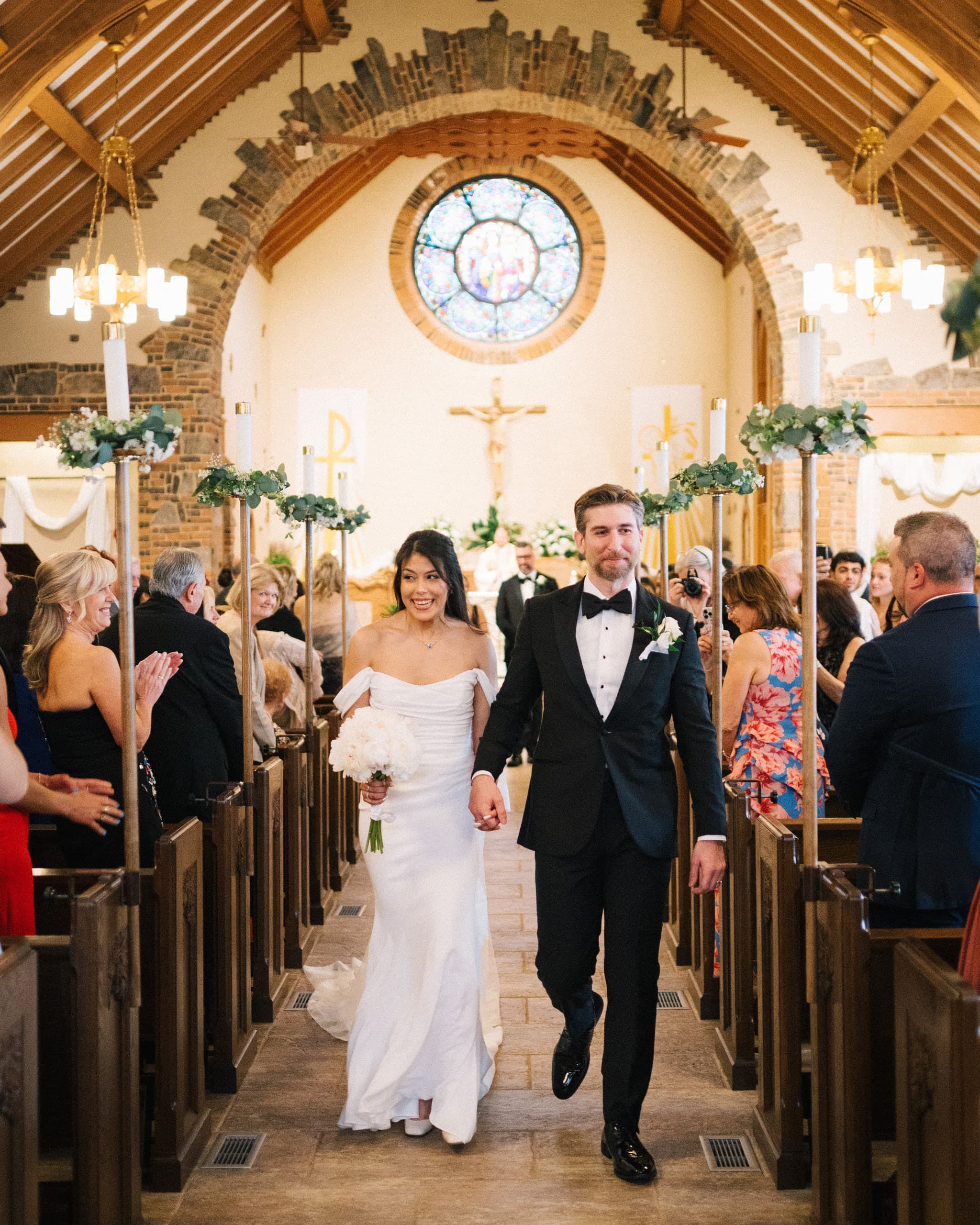 Newlyweds walking back up the aisle of a stone chapel as guests applaud