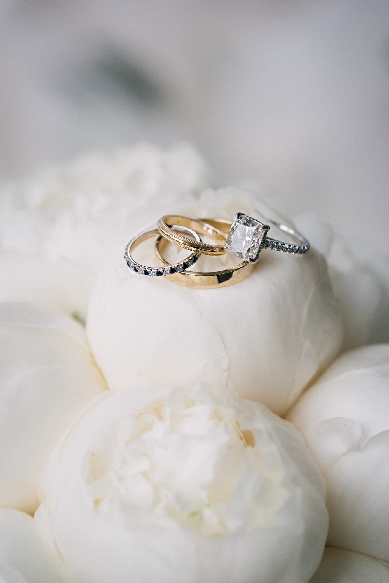 Engagement ring and wedding bands nestled on white peonies