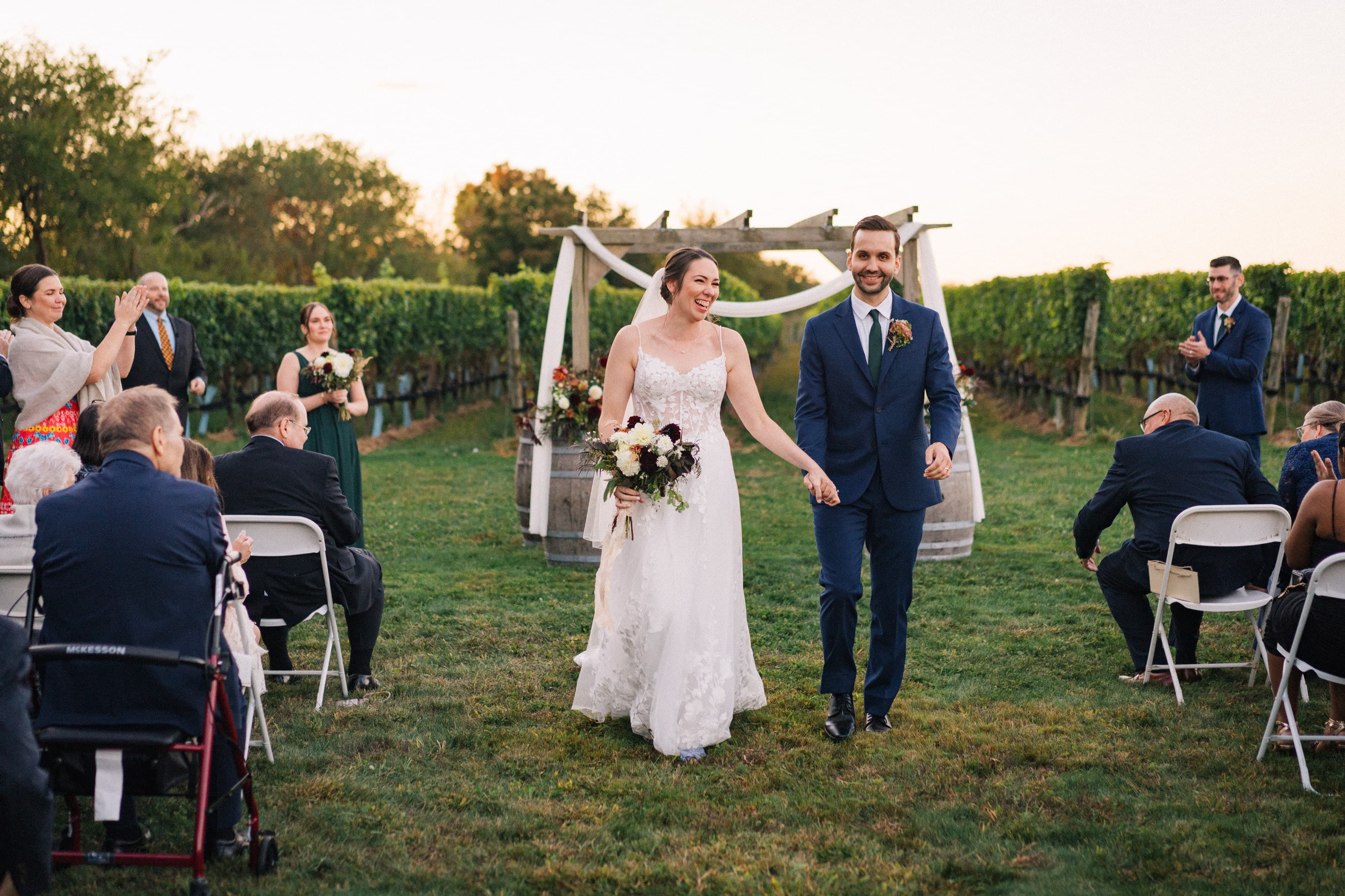 Hand in hand down the grassy vineyard aisle at golden hour