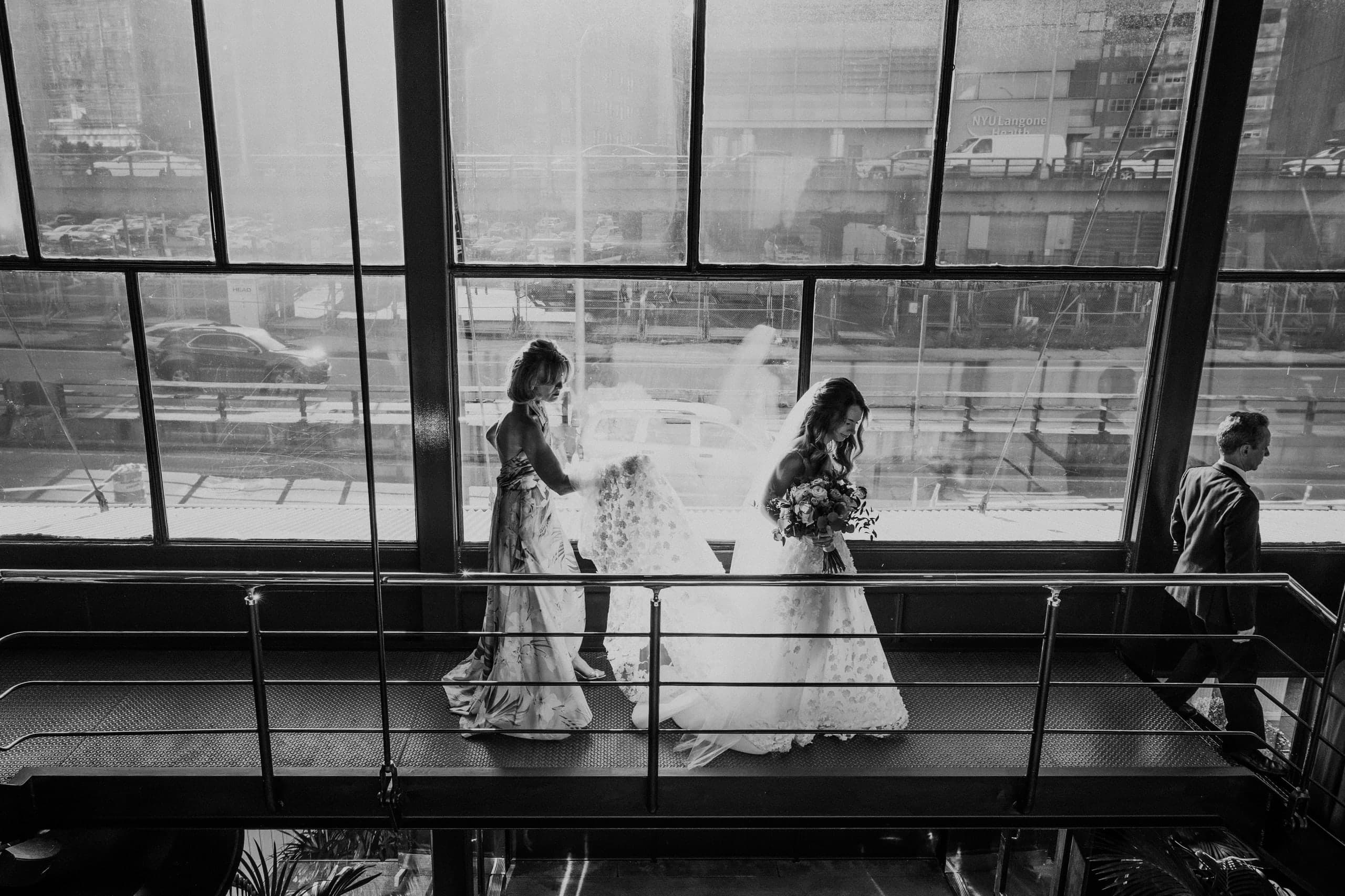 Carrying the bride's train along a catwalk above the city streets, black and white