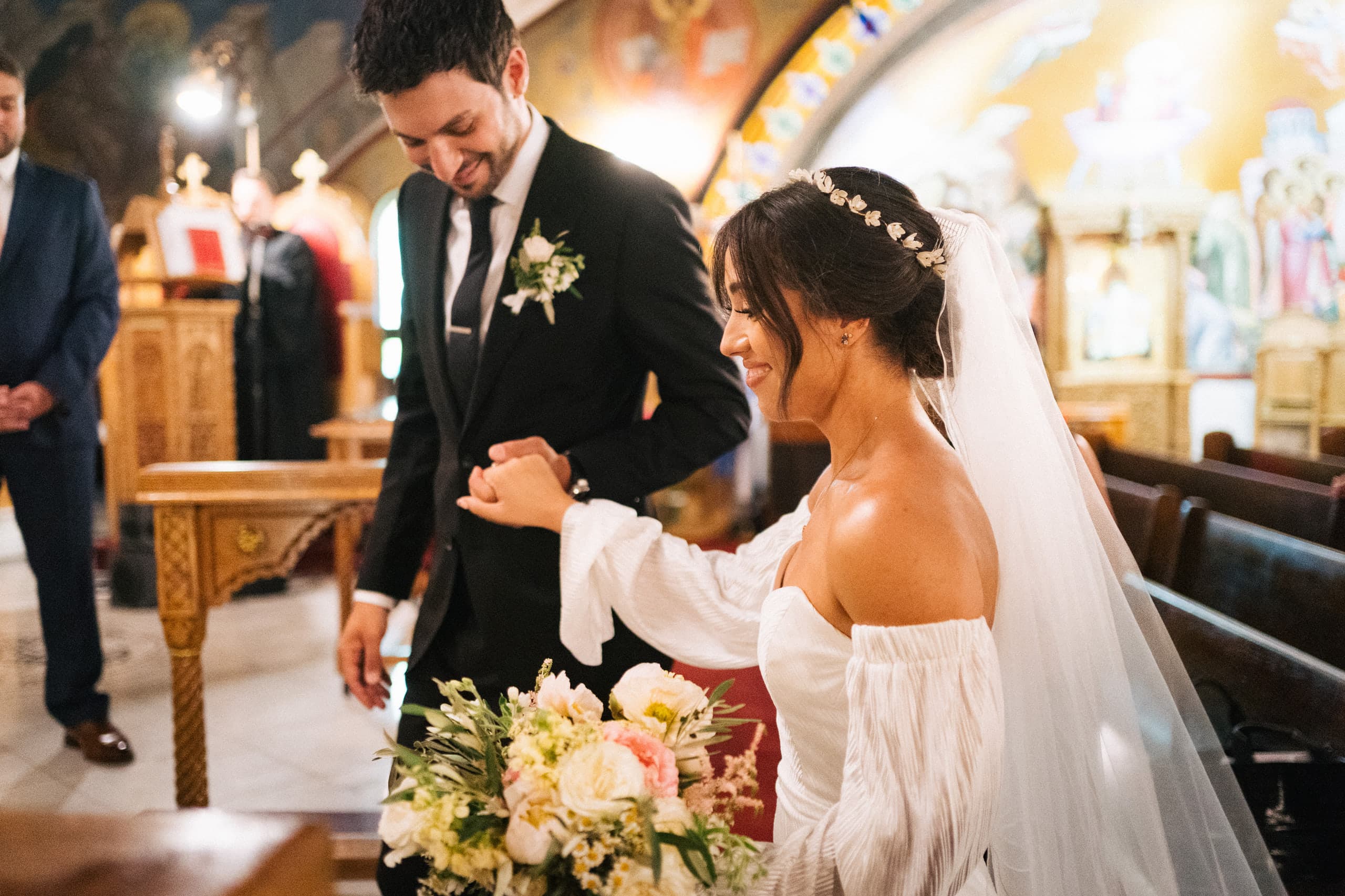 Hands joined at the altar of an ornate Orthodox church, bouquet in bloom