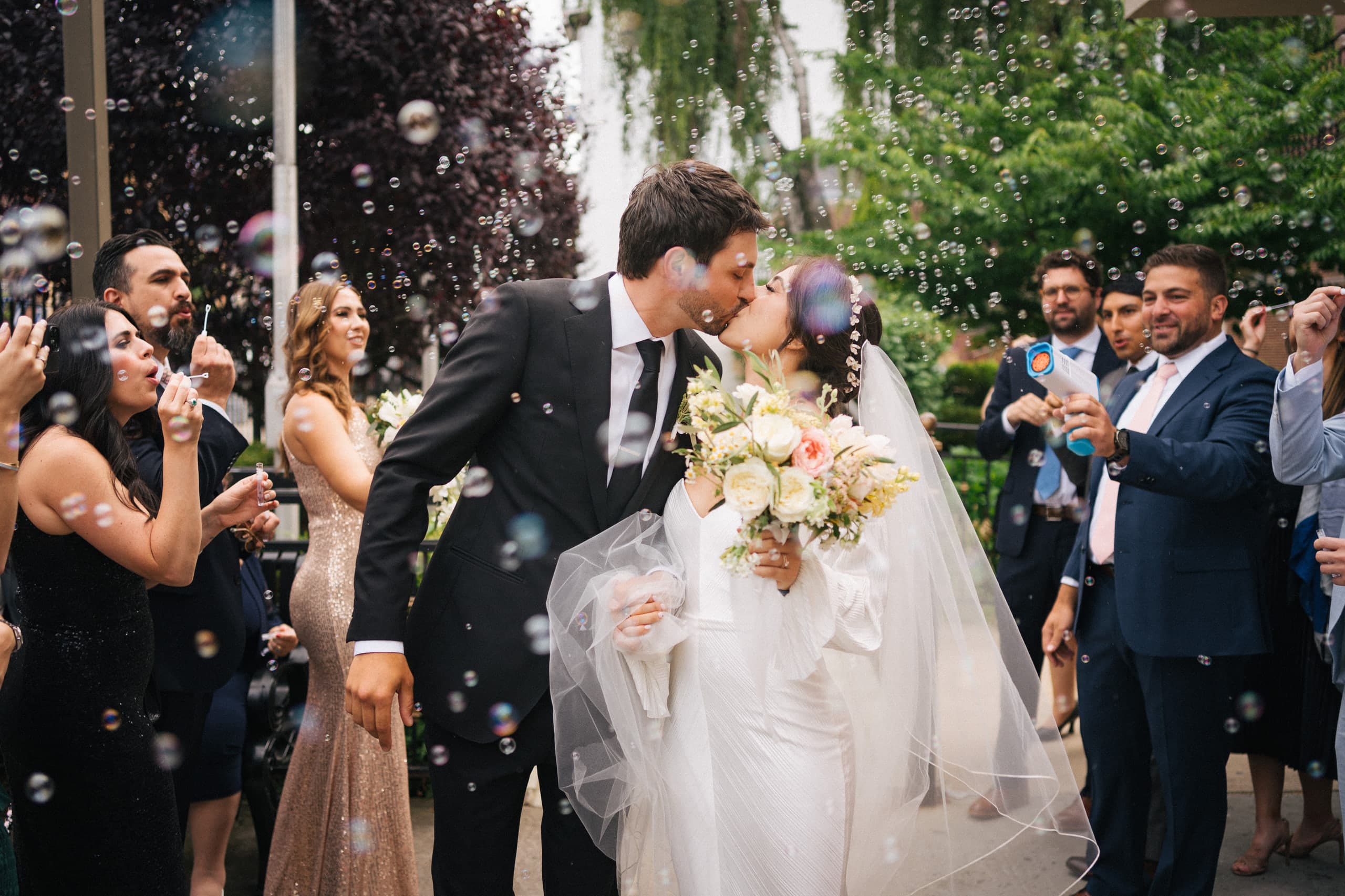 The bride pulled close for a kiss as guests fill the air with bubbles