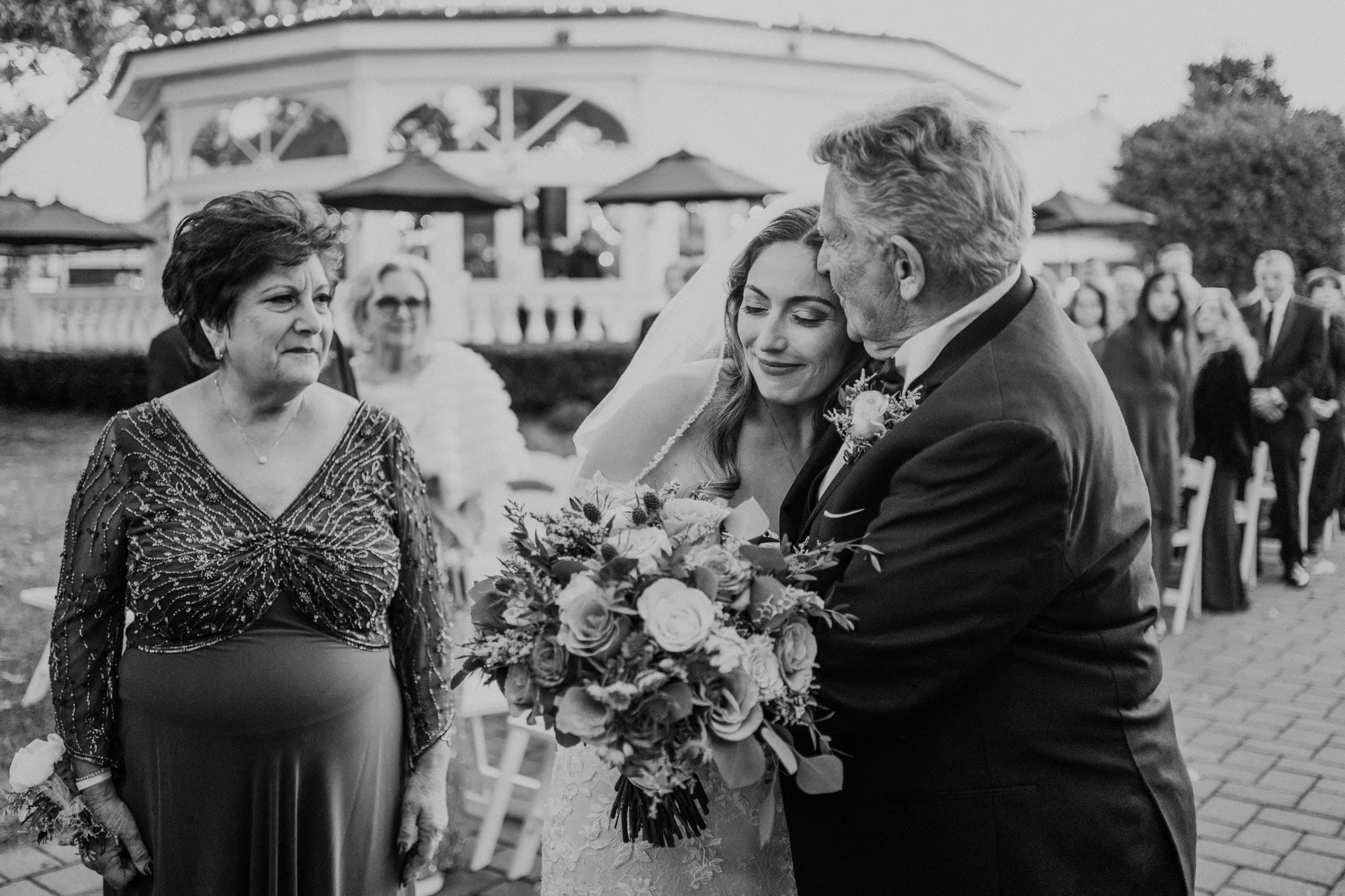 A kiss from dad at the end of the aisle as mom looks on, black and white