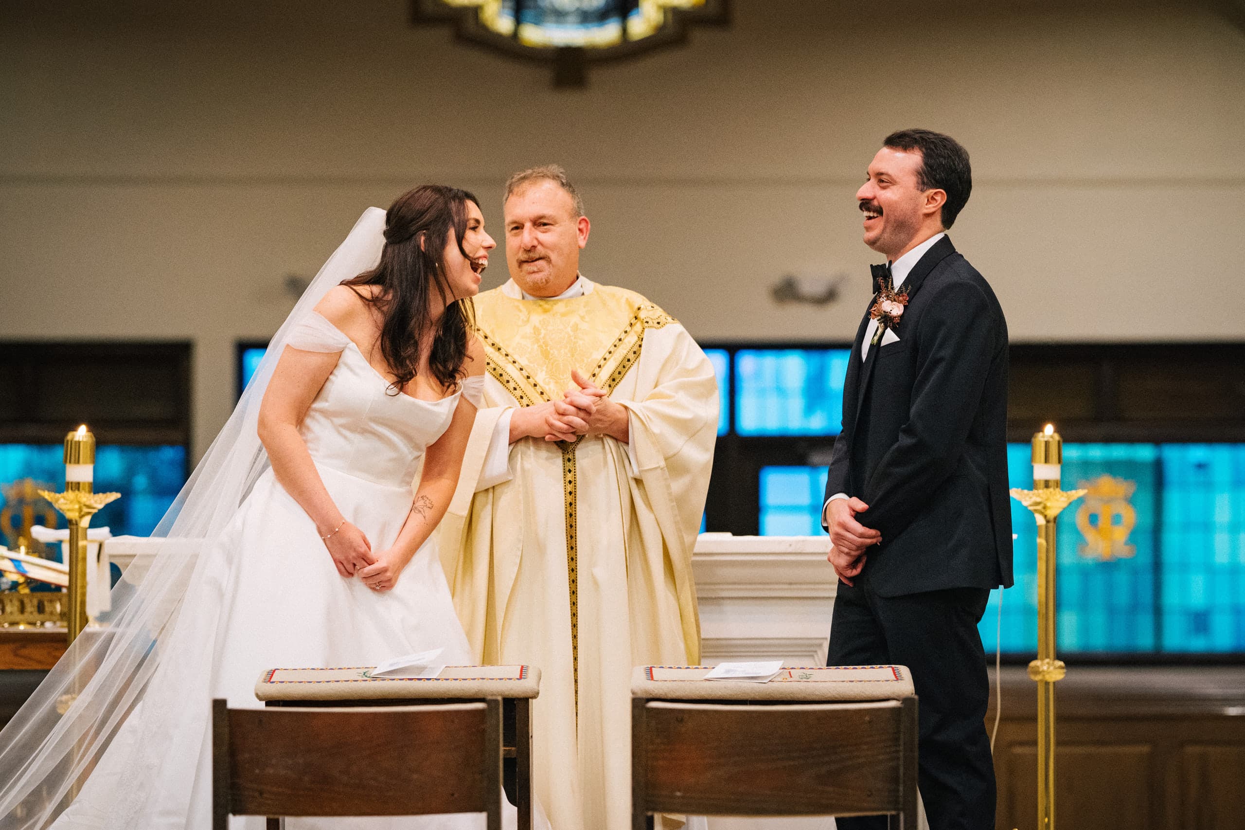 Bride and groom laughing with the priest across the altar rail