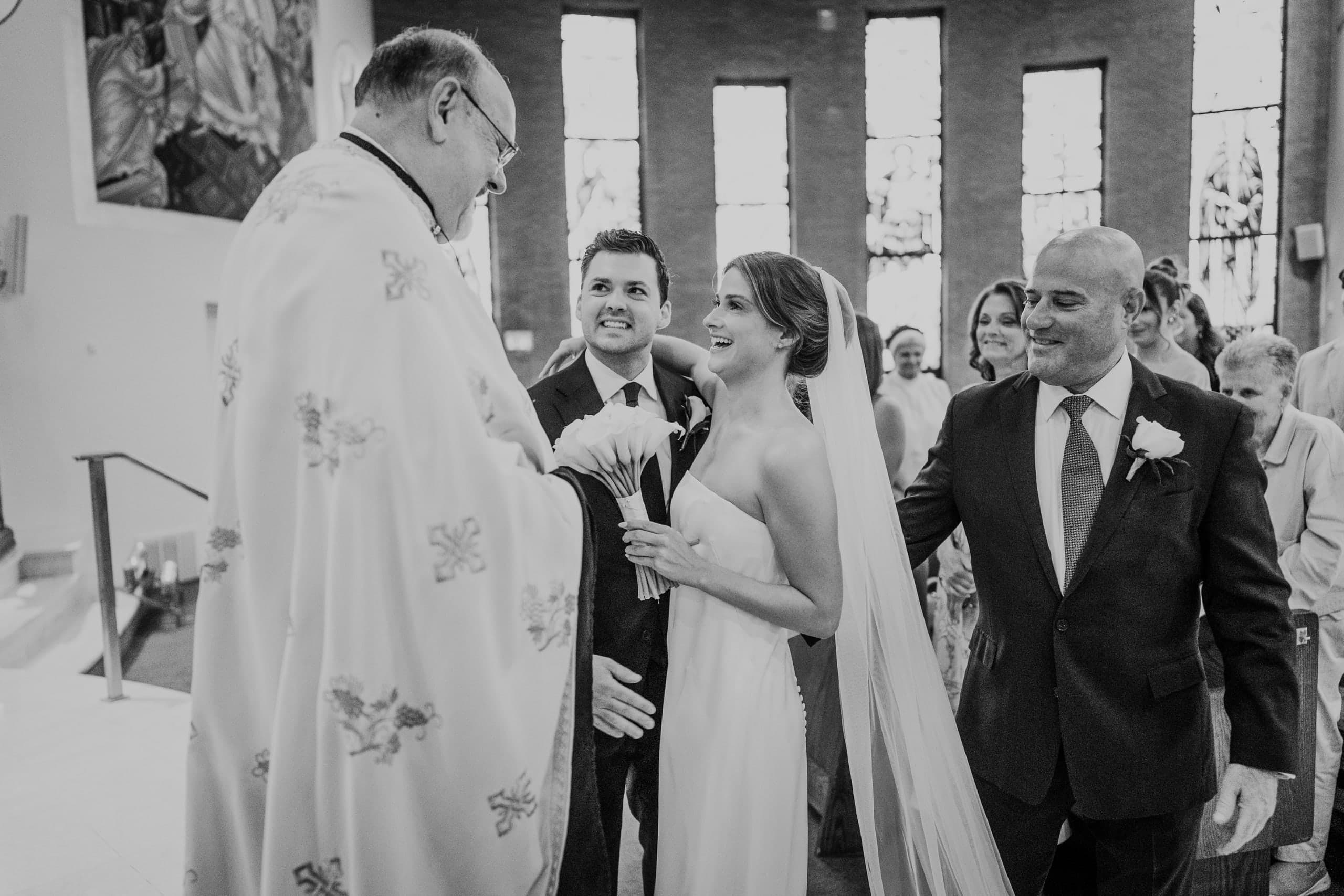 The priest welcomes the bride at the front of the church, black and white