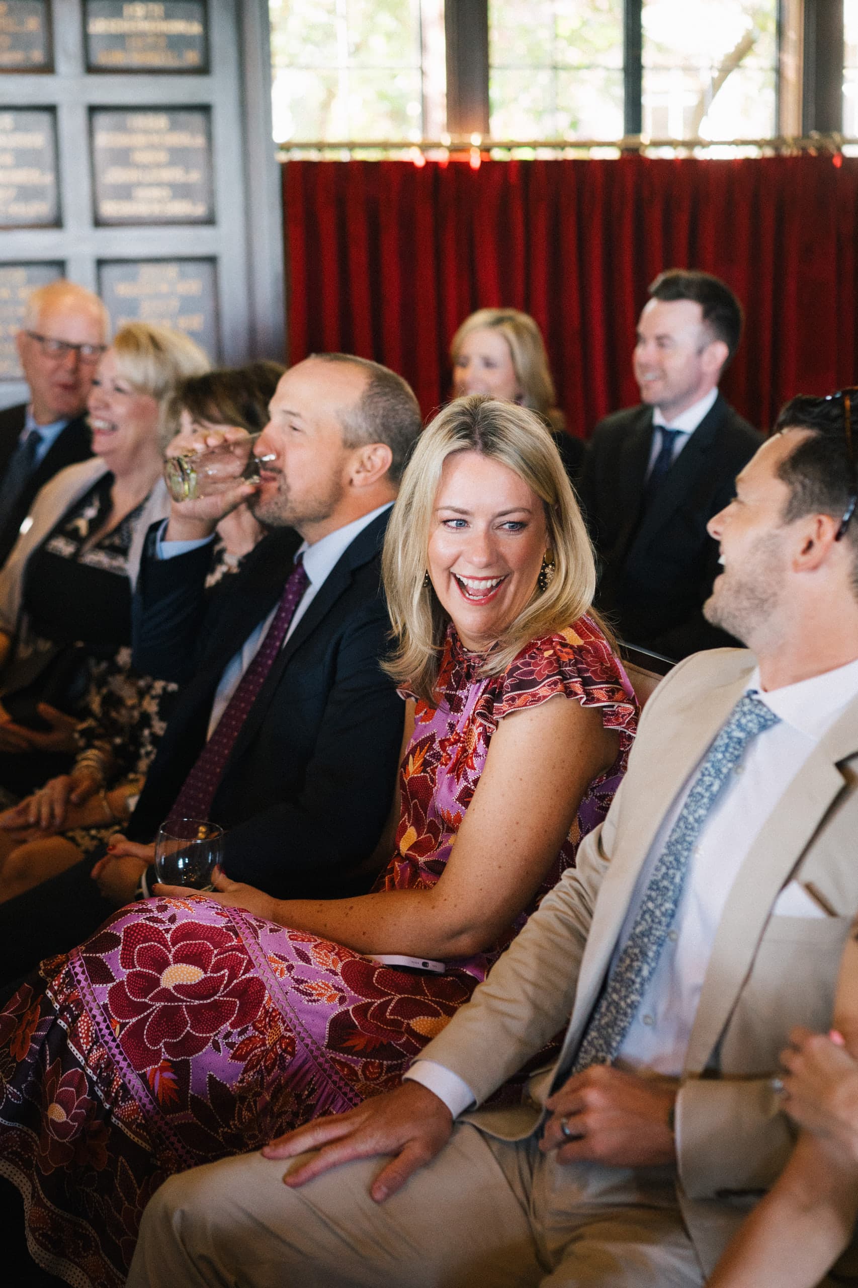 Guests laughing from their seats against a red velvet curtain