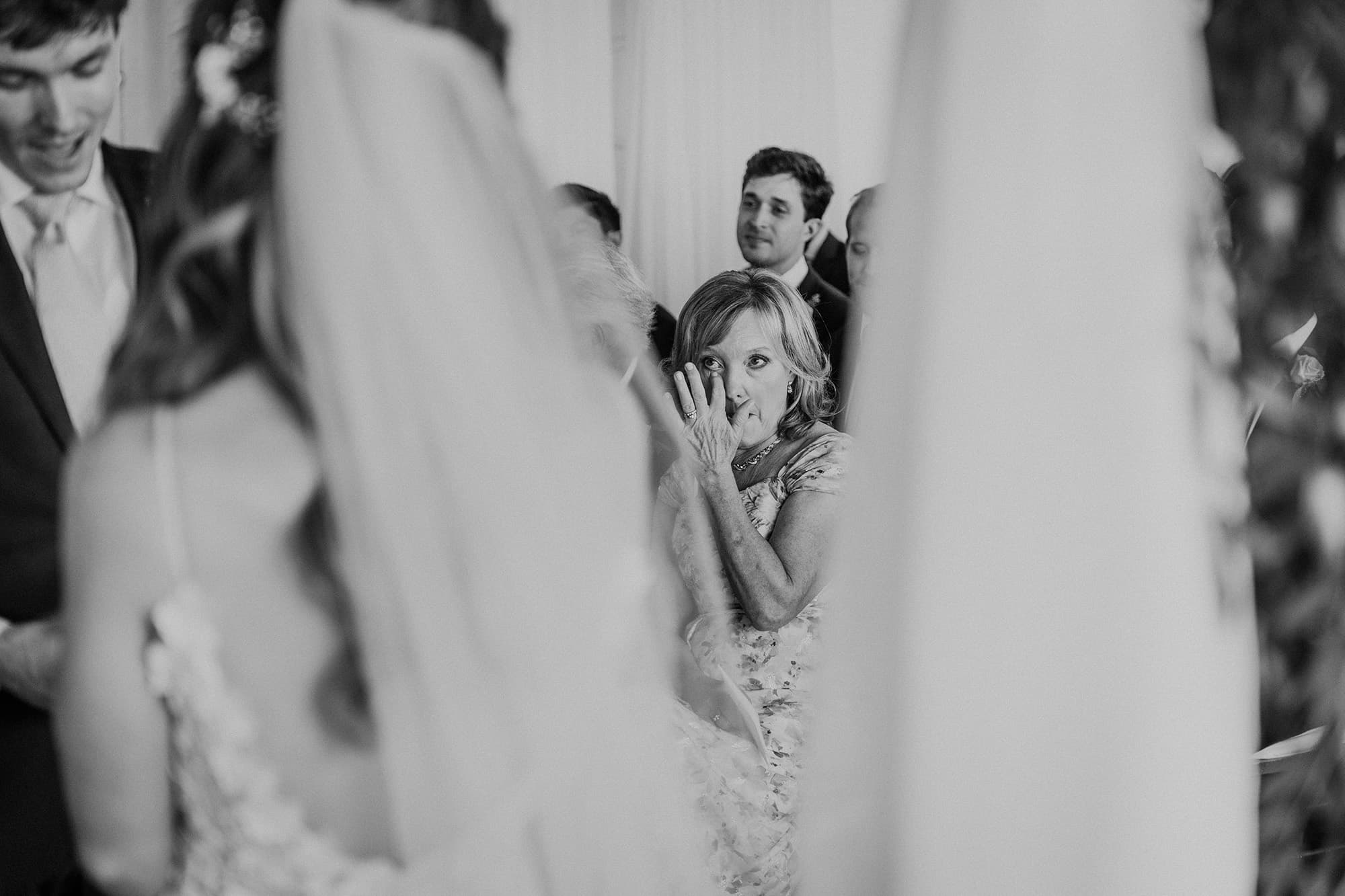 A mother wipes away tears, glimpsed past the bride's veil, black and white