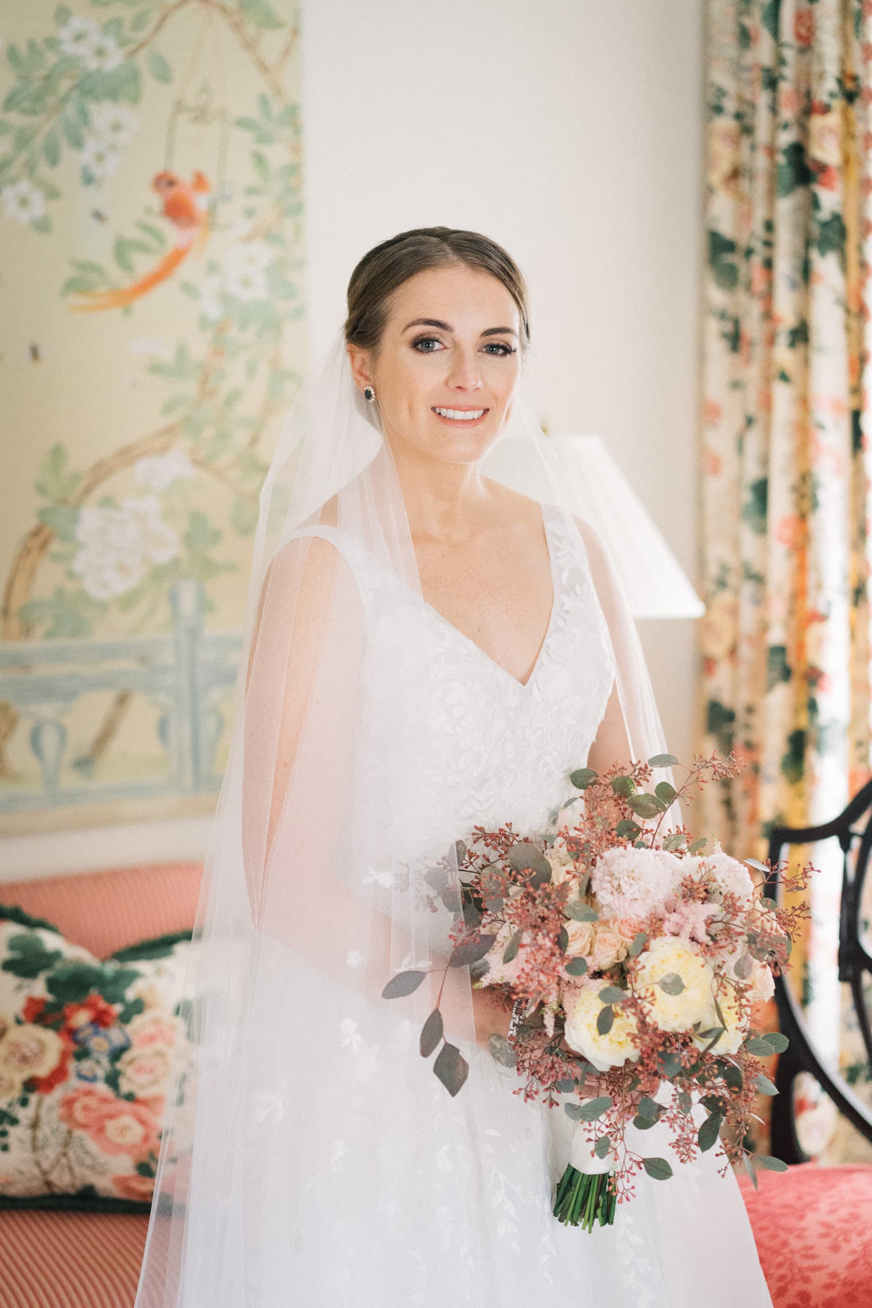Veiled bride holding a blush bouquet before chinoiserie panels and floral drapes