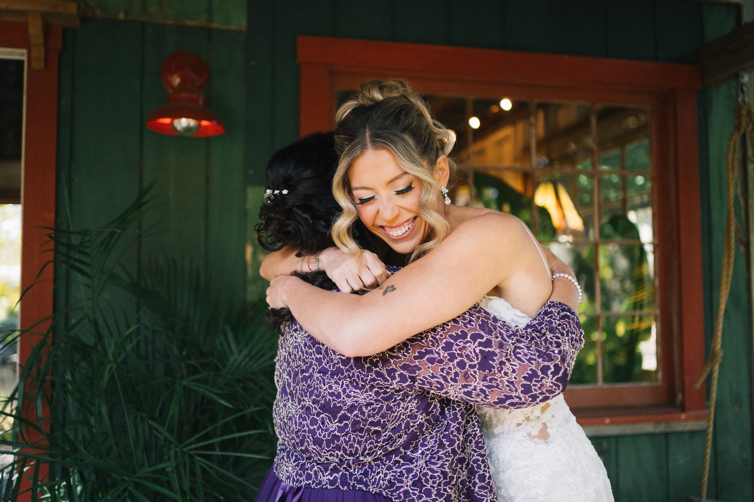 Bride wrapping her mother in a tight hug on the porch of a green wooden cottage
