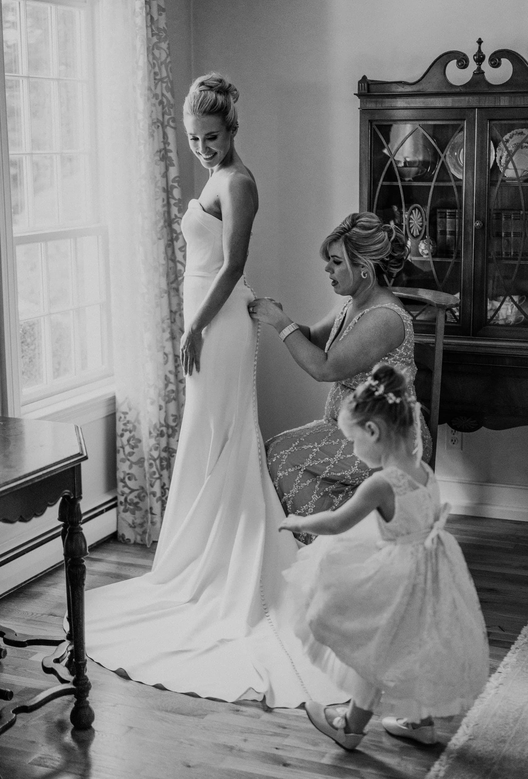 Flower girl helping arrange the bride's train in window light, black and white