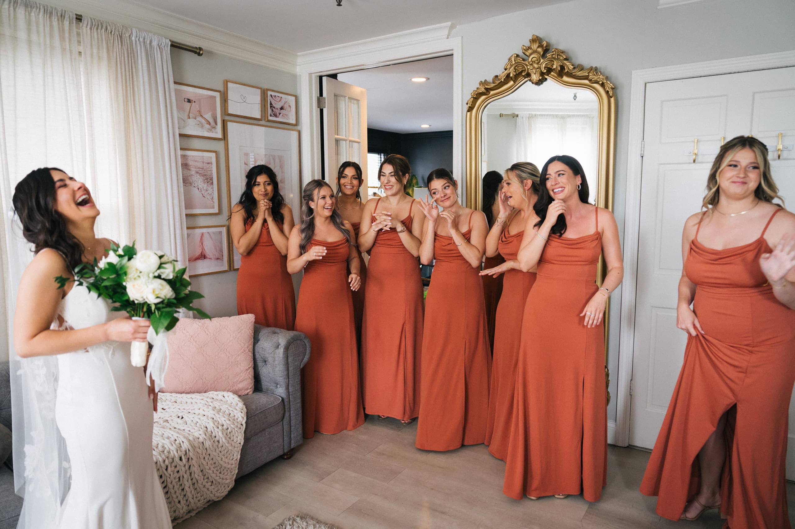 Bride laughing with her bouquet as bridesmaids in rust gowns applaud her reveal