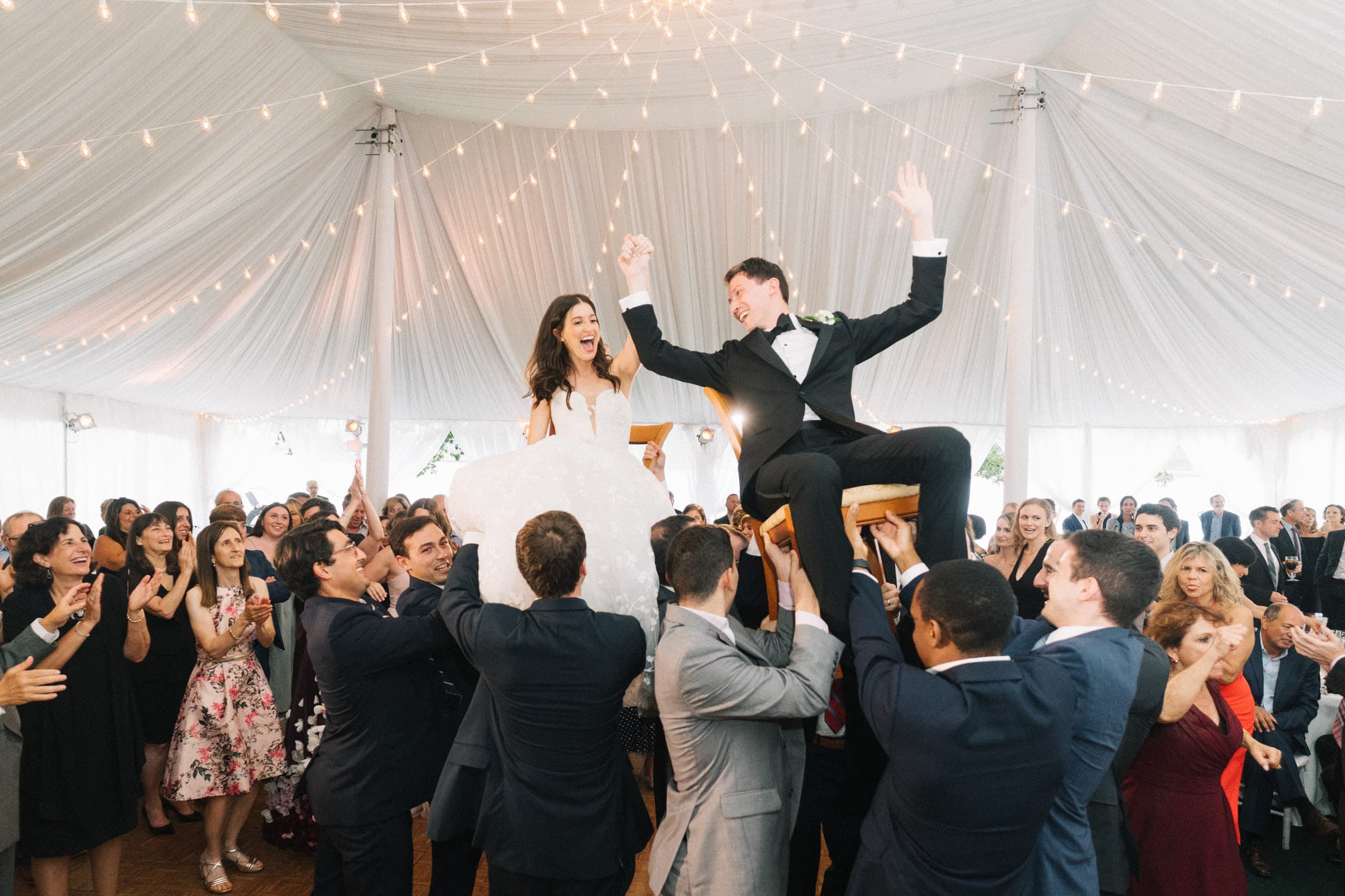 Hoisted on chairs for the hora beneath the string-lit tent
