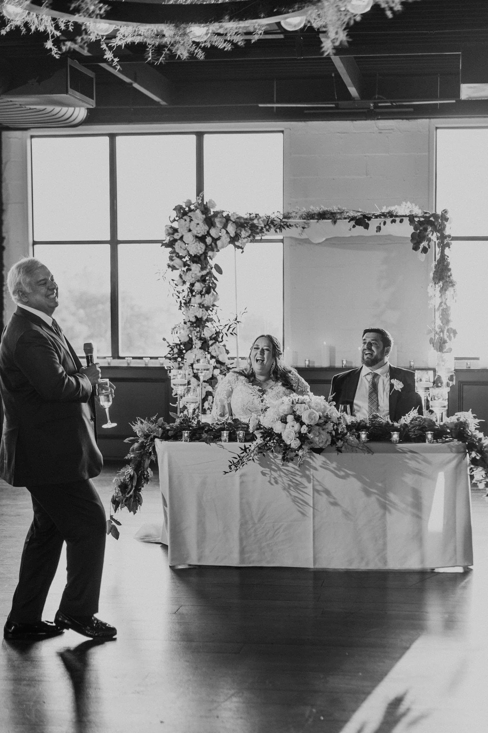 A toast to the couple framed by the flower arch, black and white