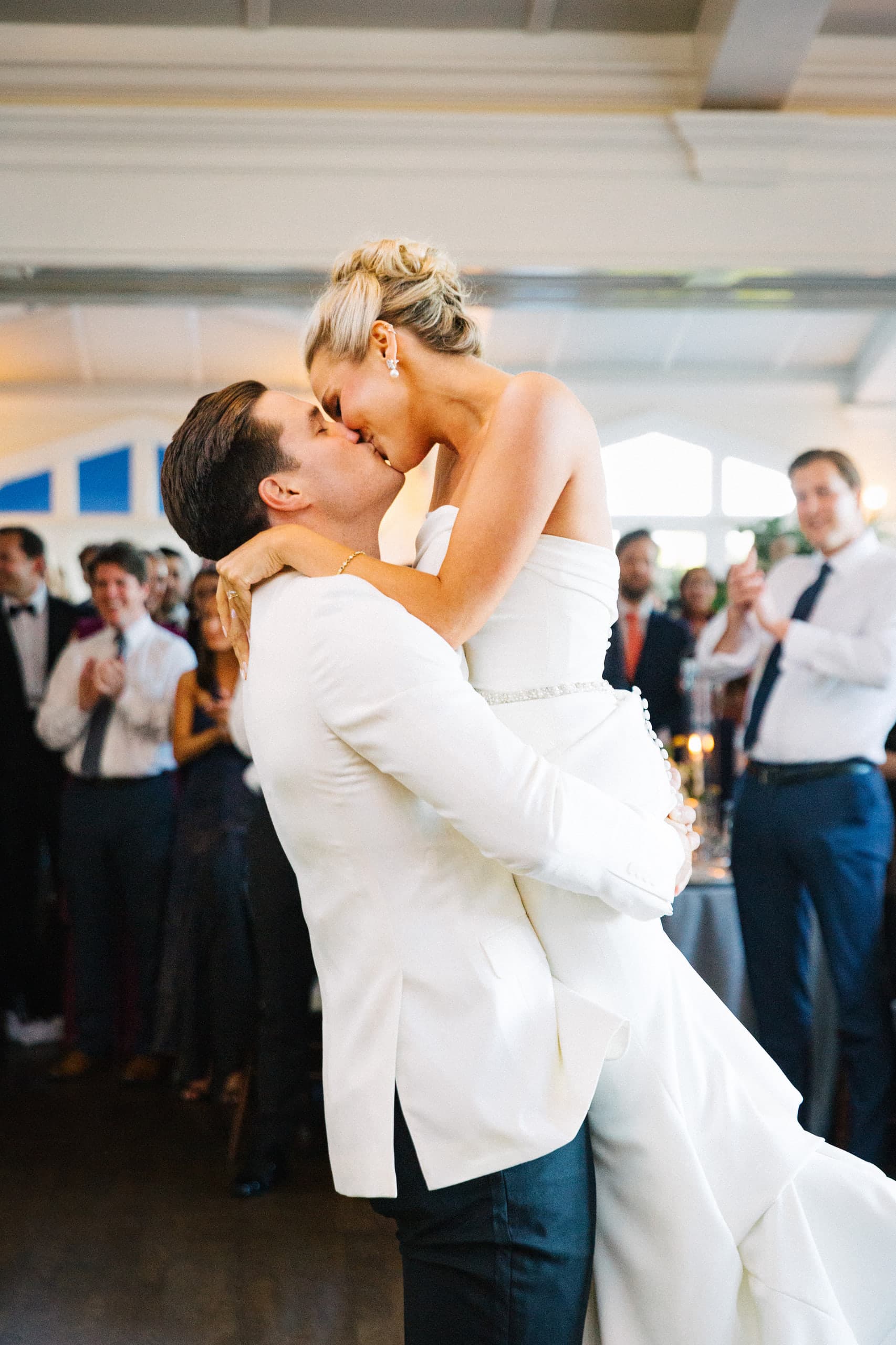 The groom lifts his bride into a kiss as the room applauds
