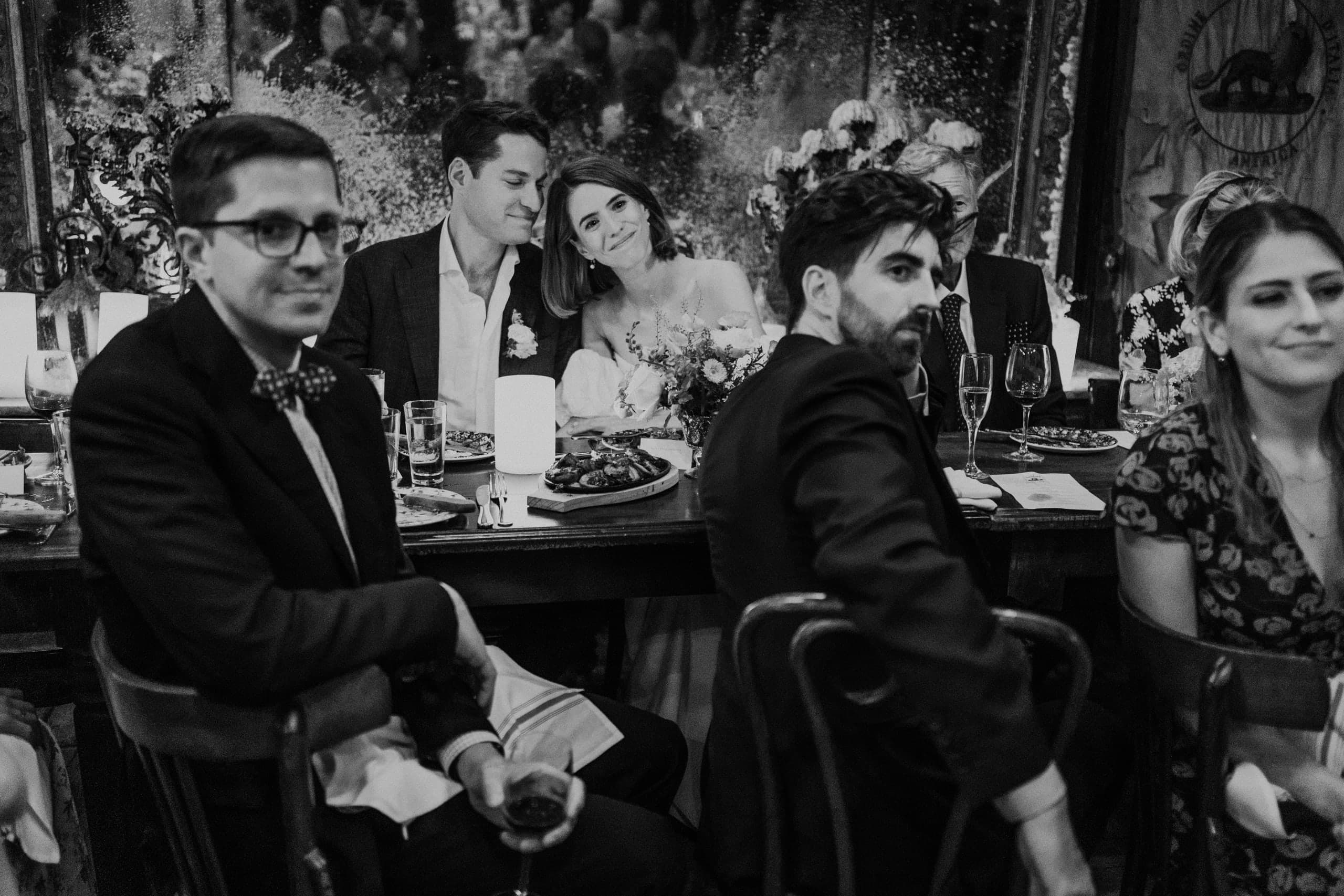 A quiet lean on his shoulder down the long dinner table, black and white