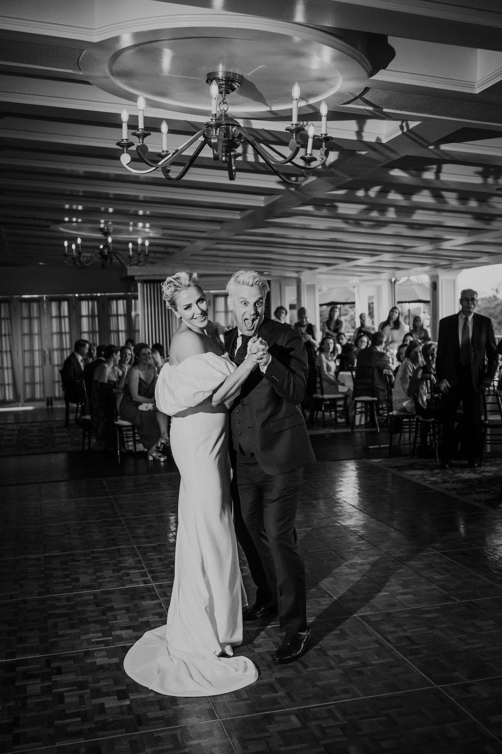 A dance beneath the chandelier as the room looks on, black and white