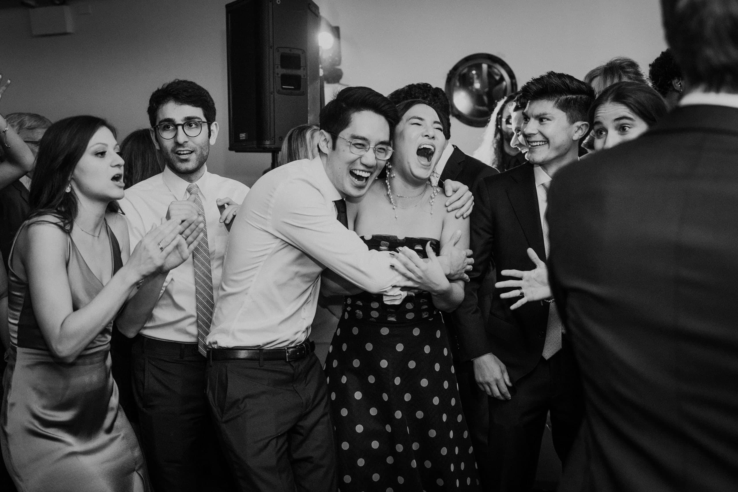 Friends collapse into a laughing group hug by the speakers, black and white