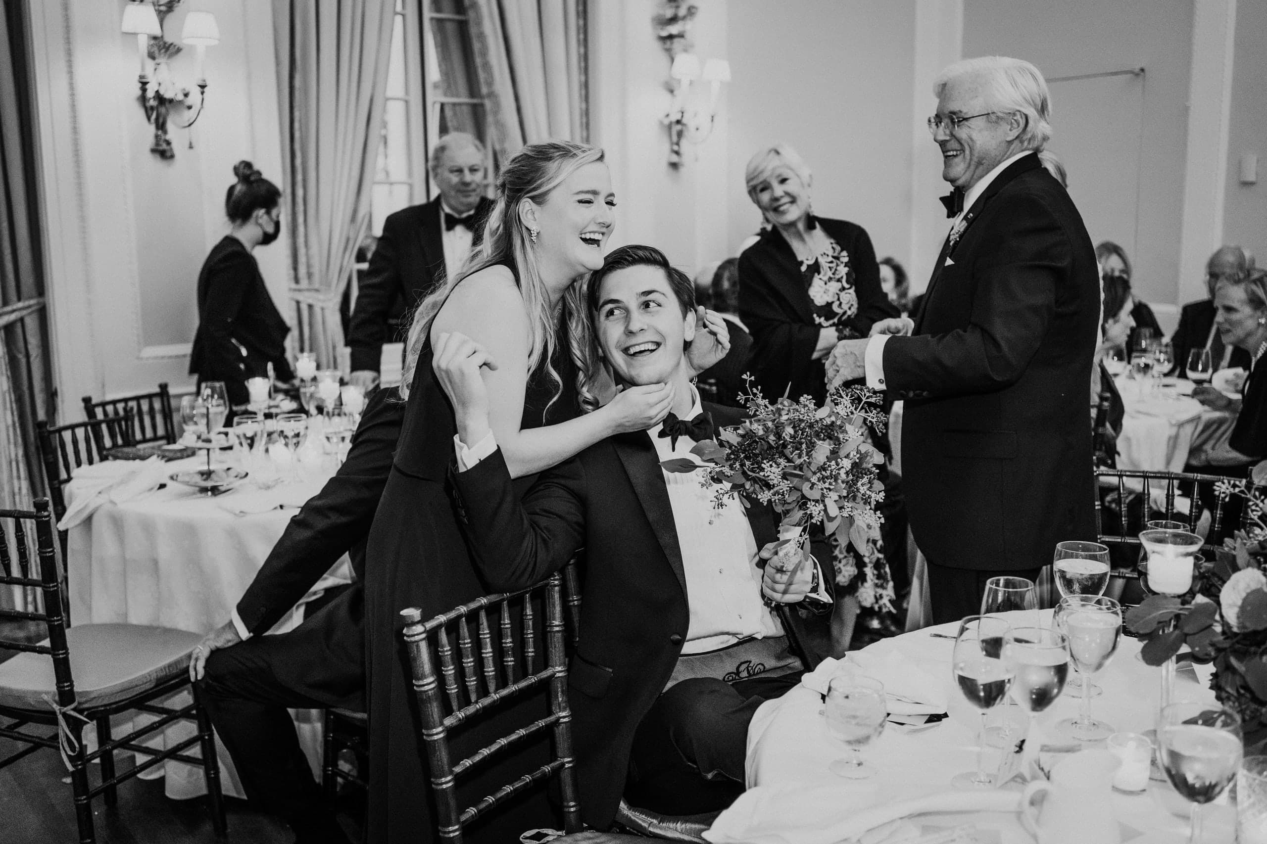Laughter draped over his chair as family gathers round, black and white