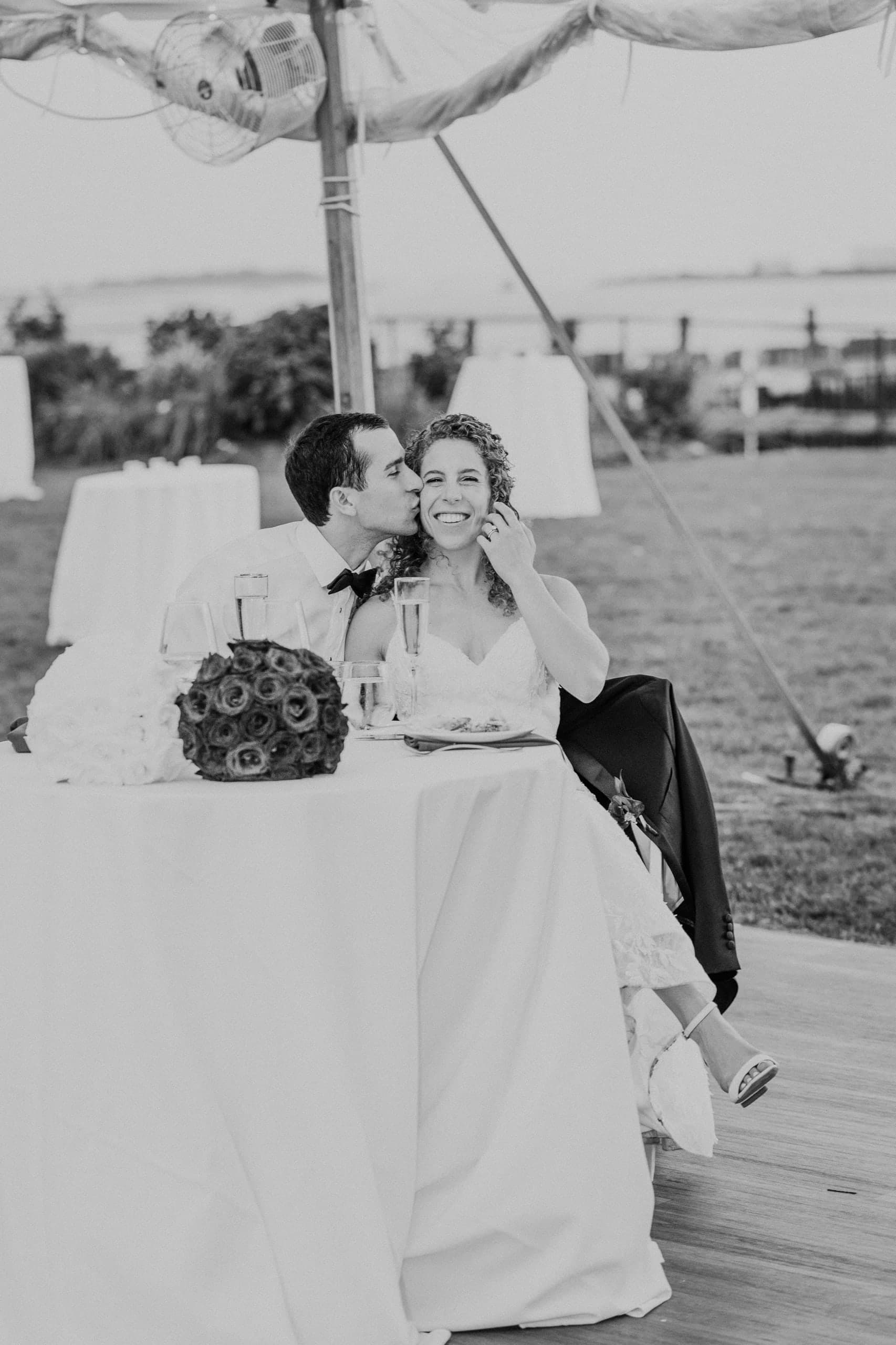 A kiss on the cheek at the sweetheart table by the water, black and white