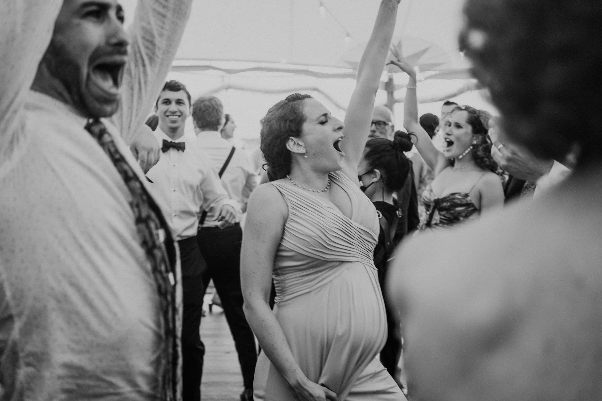 An expectant guest sings along, hand on her belly, black and white