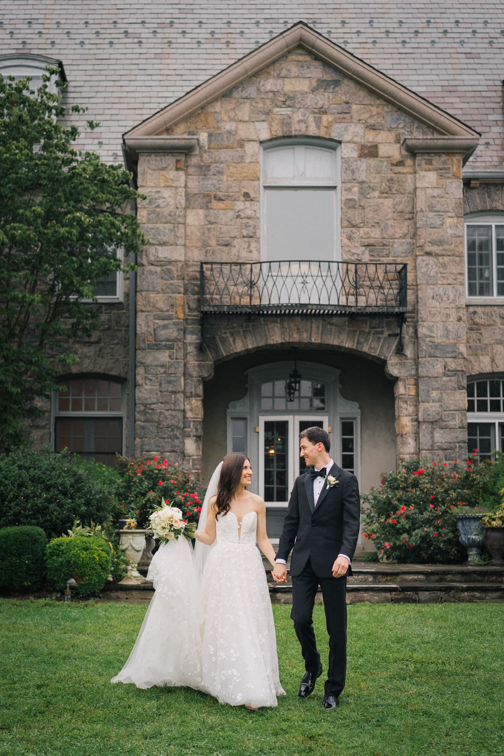Hand in hand on the lawn before a stone manor, roses in bloom