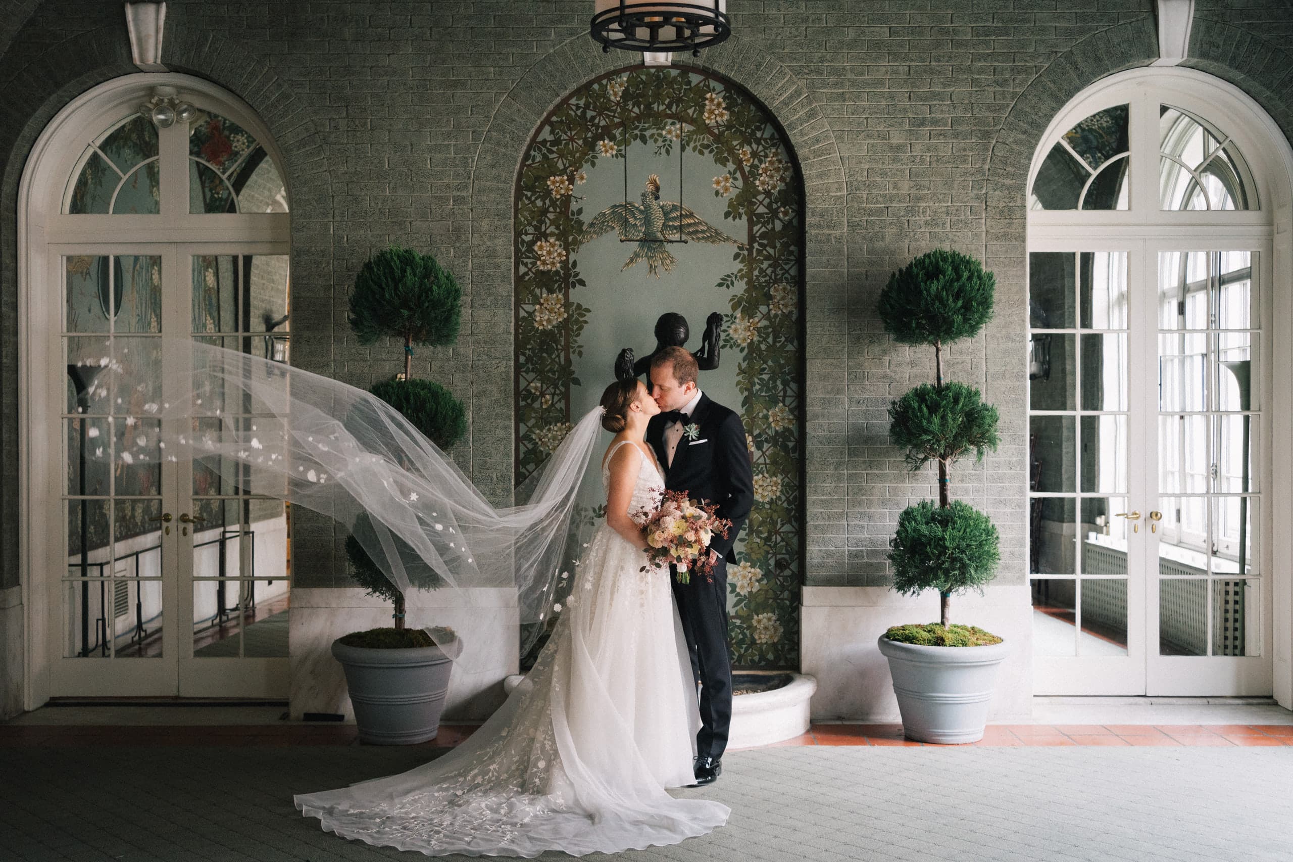 A kiss beneath the arched loggia, the veil drifting past the topiaries