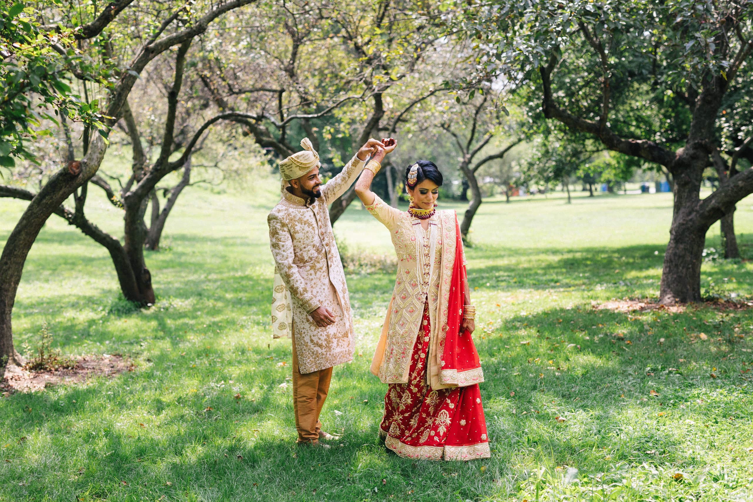 A twirl under the orchard trees in red and gold wedding attire