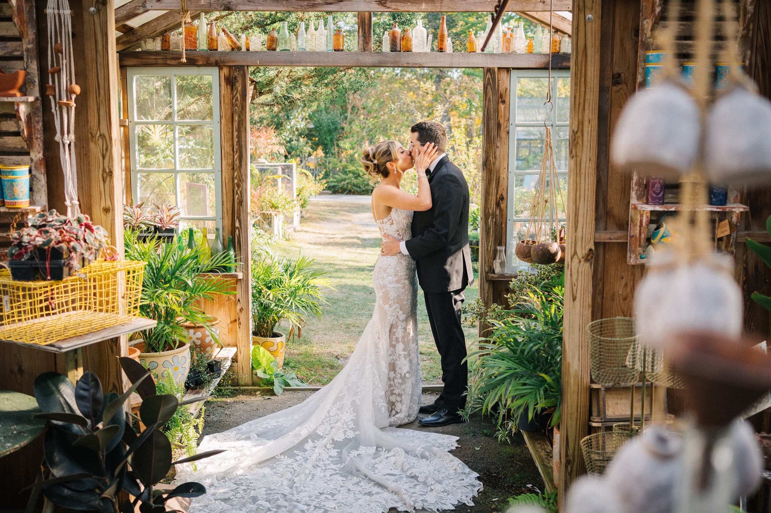 A kiss in a rustic greenhouse, the lace train spilling across the floor