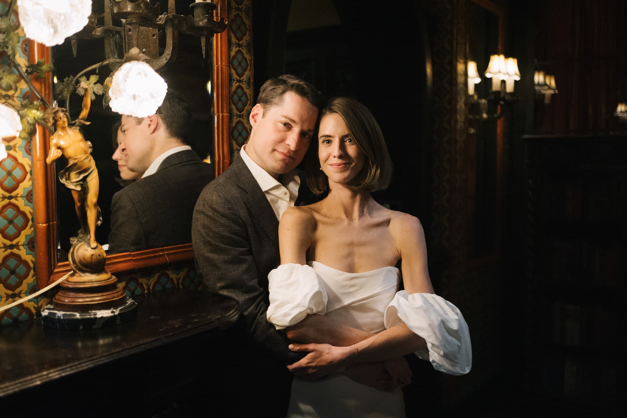 An embrace beside the gilded mirror in a dim, ornate room