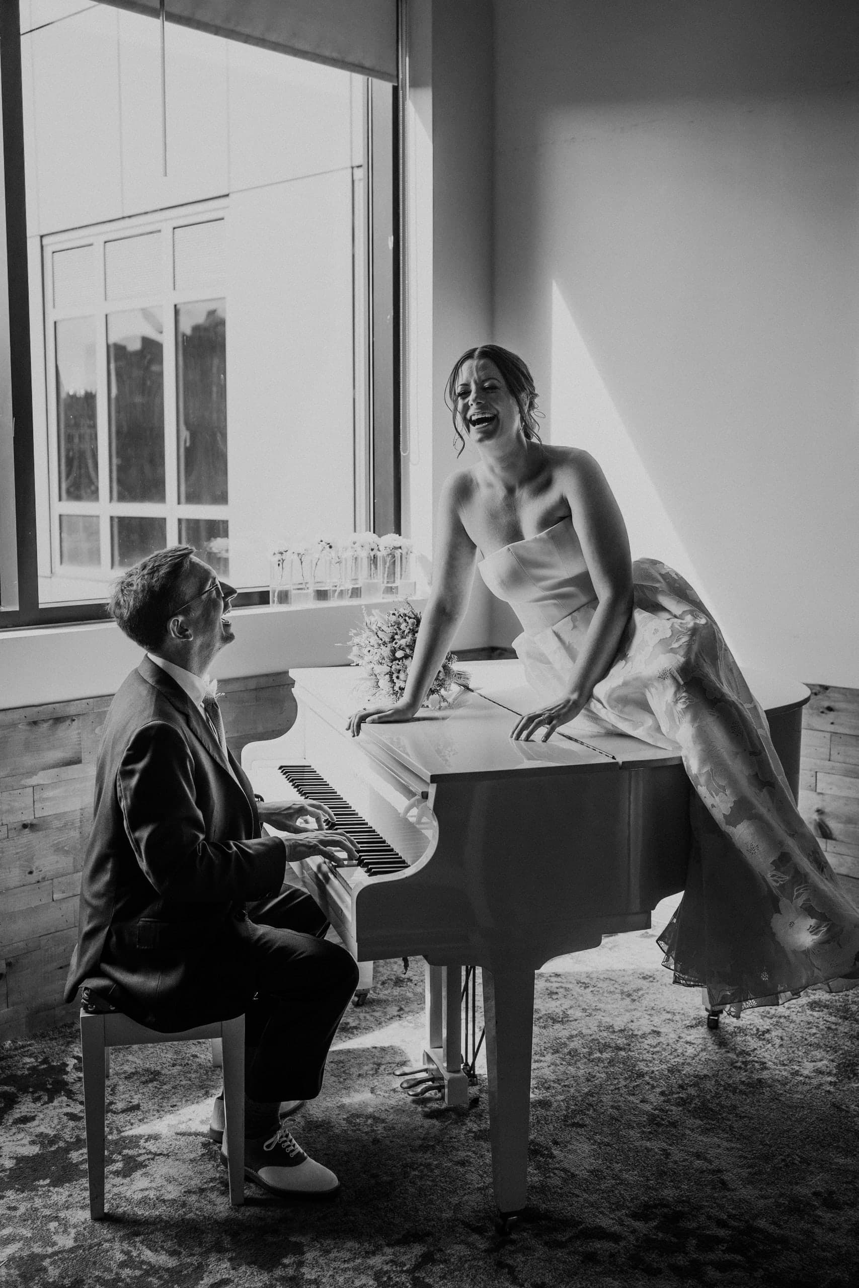 Perched on the grand piano, laughing as he plays, in black and white